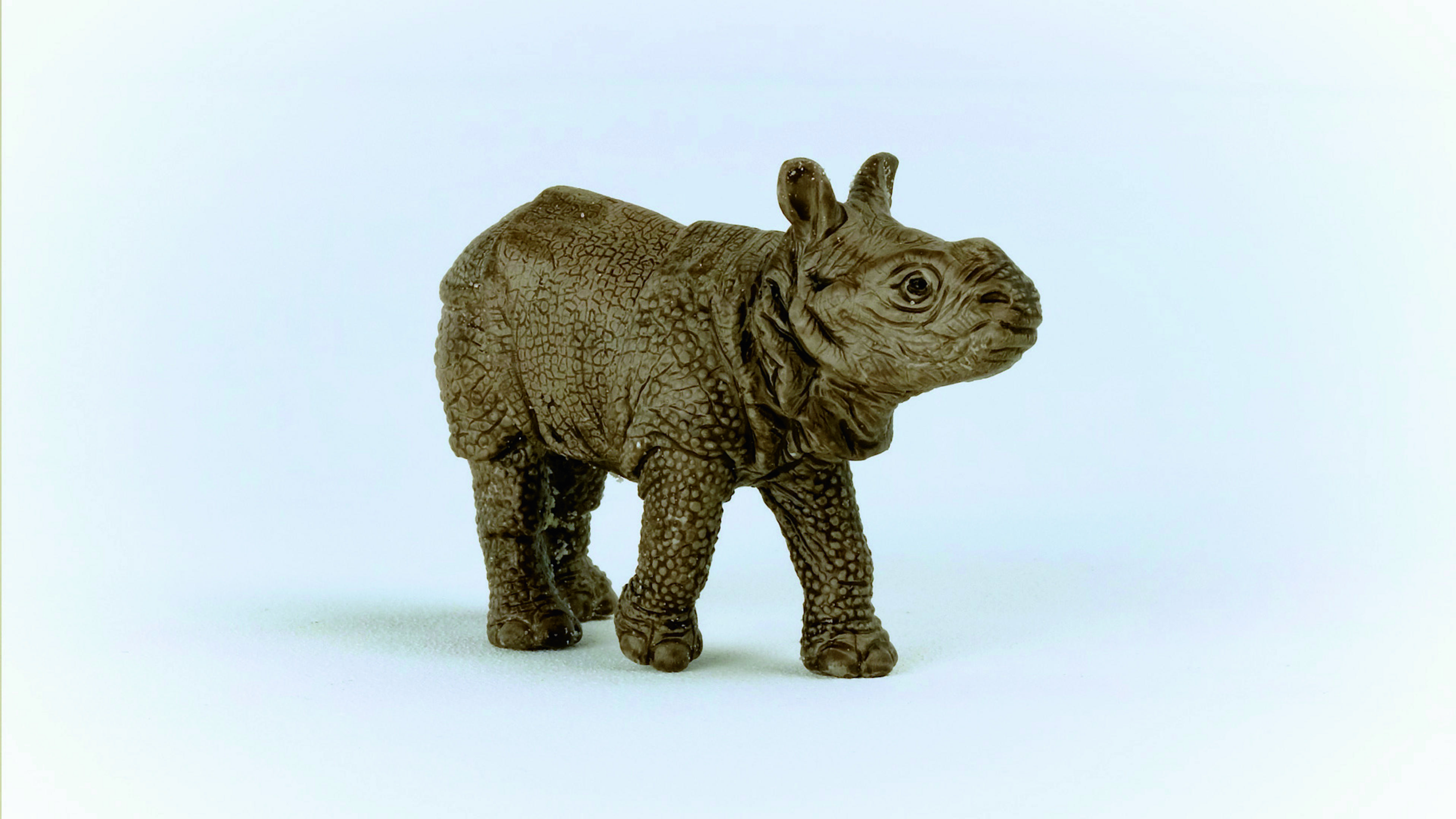 Un petit jouet de rhinocéros debout sur une surface blanche.