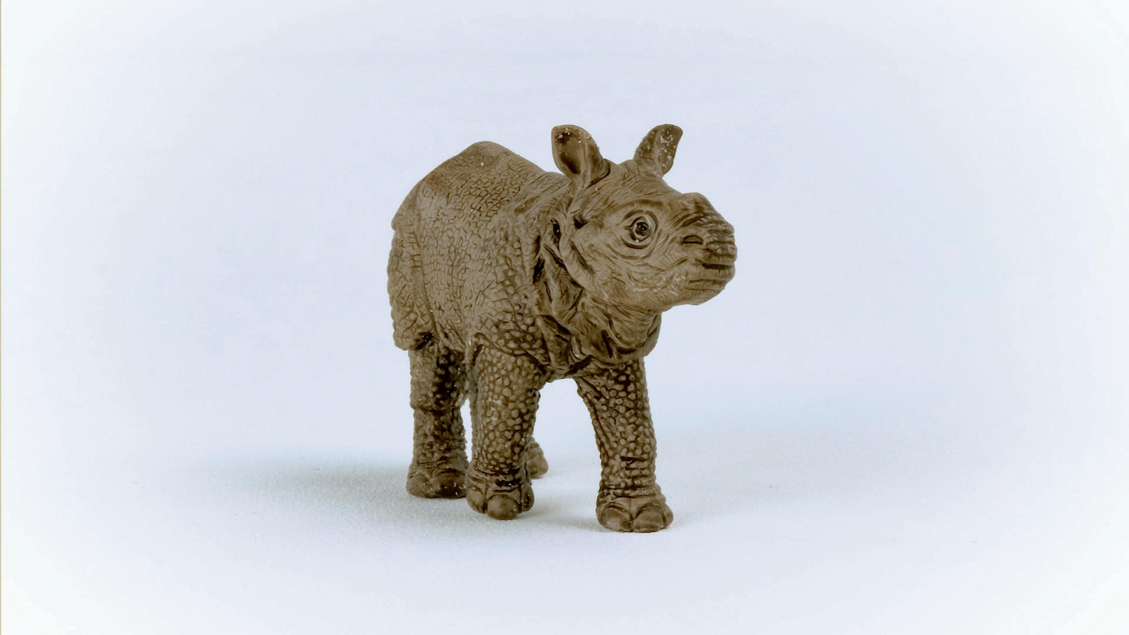 Une figurine de jouet de rhinocéros marron debout sur un fond blanc.