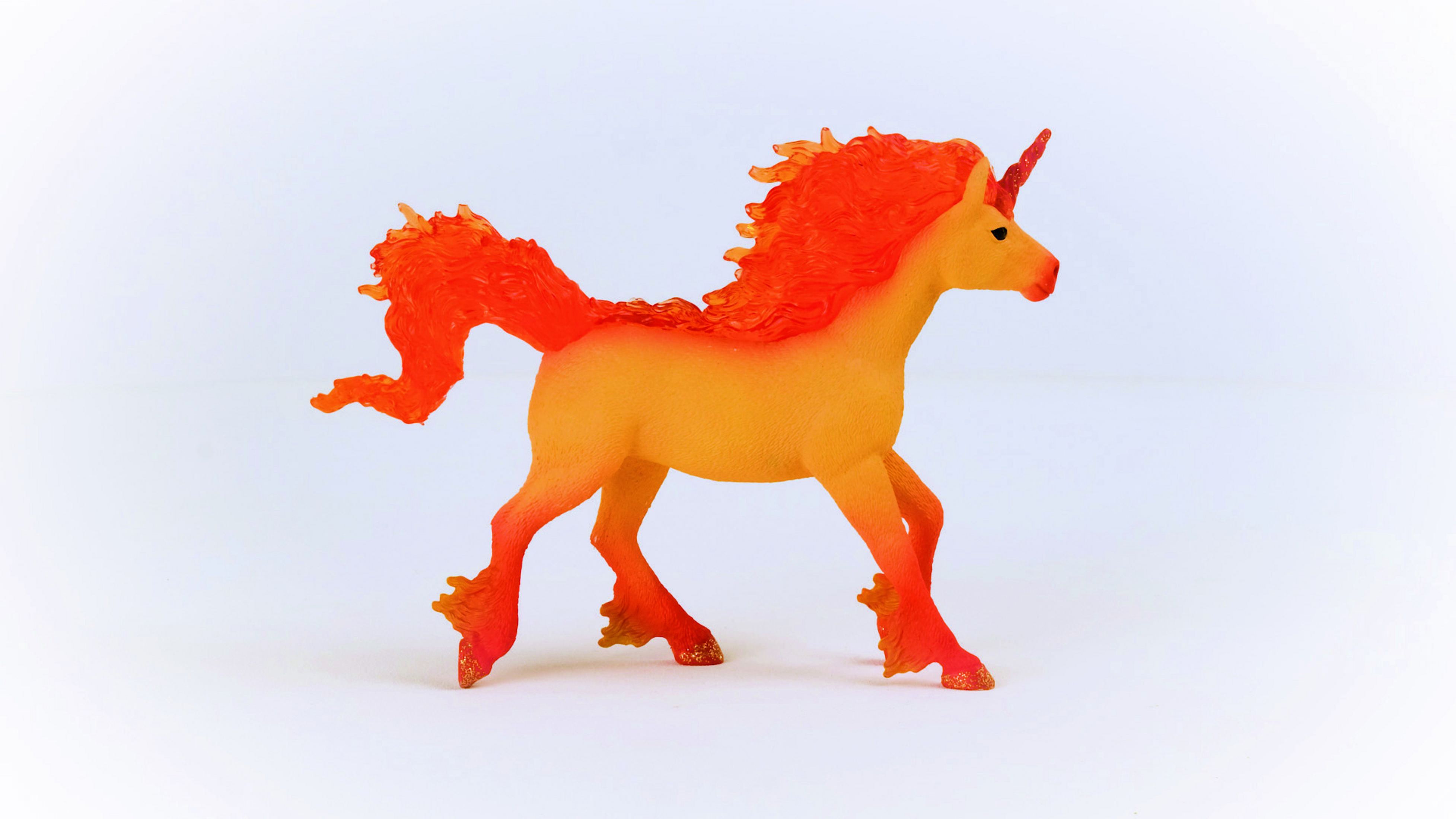 Un giocattolo unicorno arancione e giallo su sfondo bianco, con criniera e coda arancioni.
