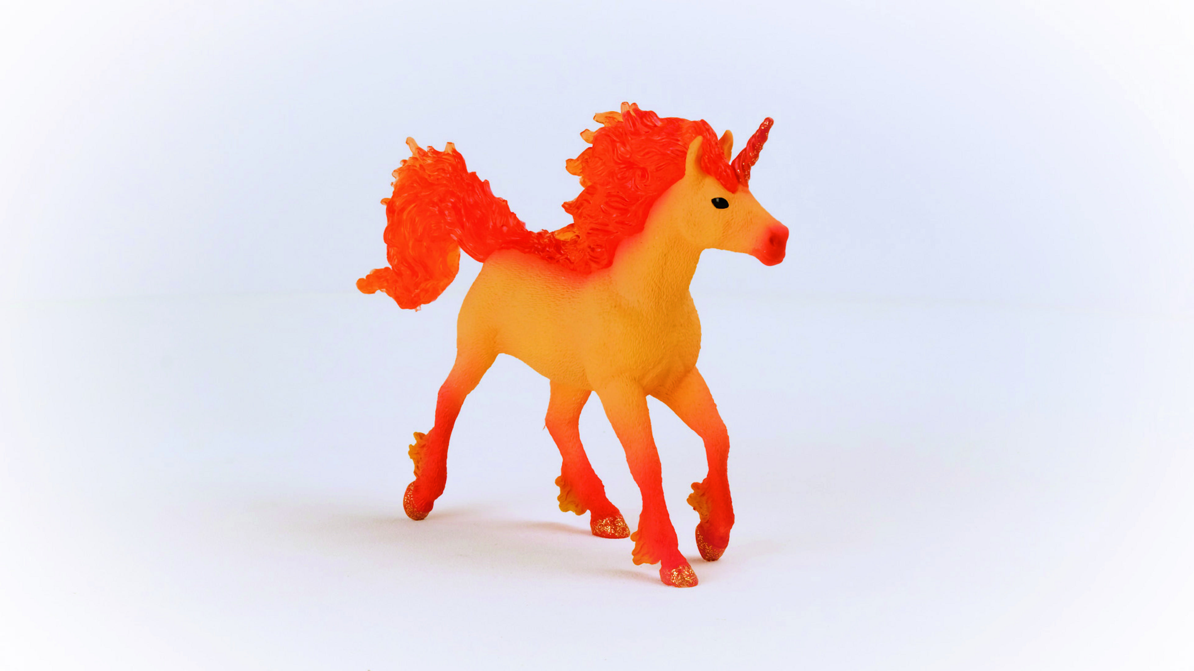 Una statuetta di unicorno giocattolo. Ha una criniera, una coda e zampe arancioni. Il corpo è giallo.