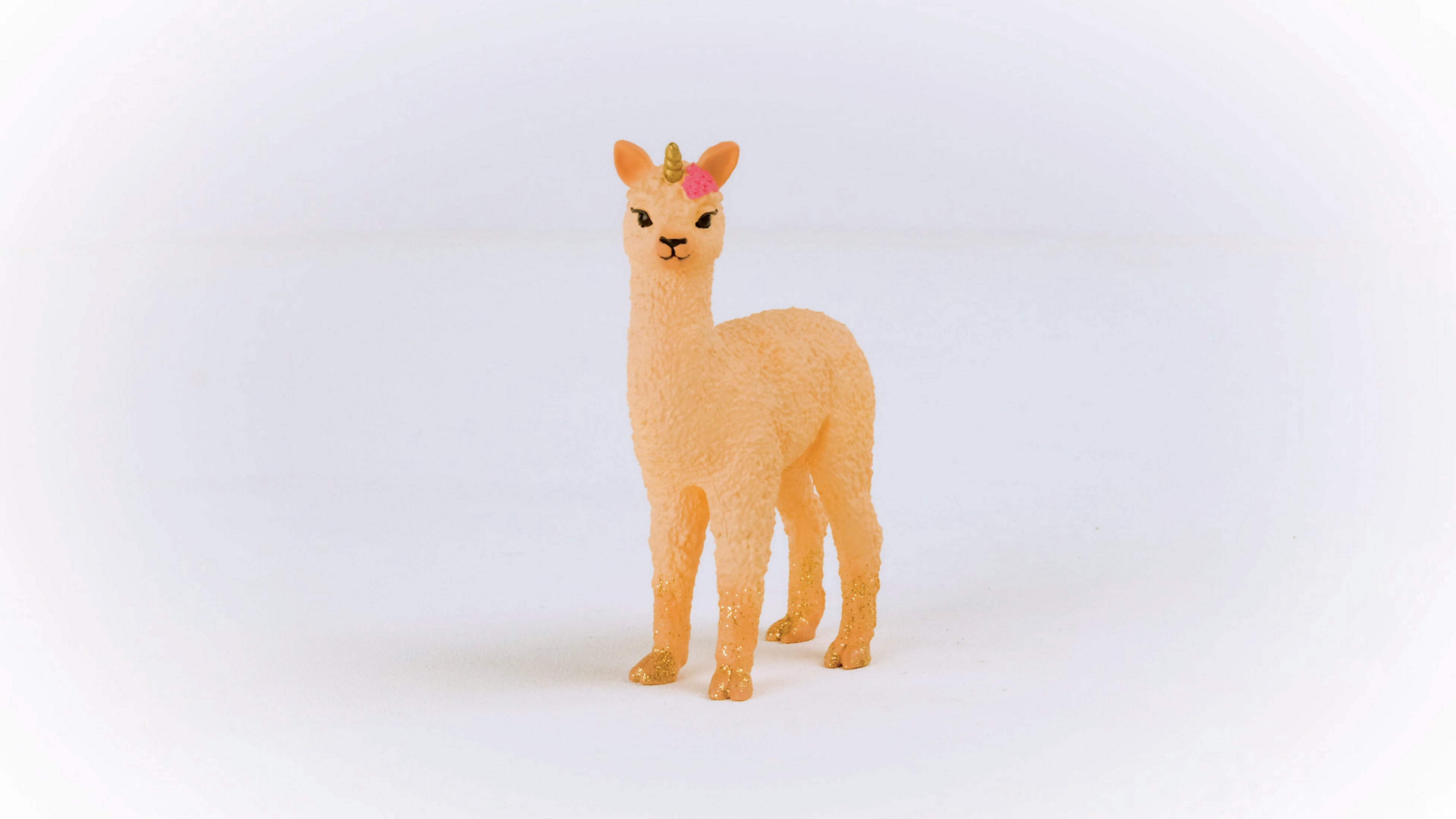 Una statuina a forma di lama giocattolo con un corno e un fiore sulla testa. Su una superficie bianca.