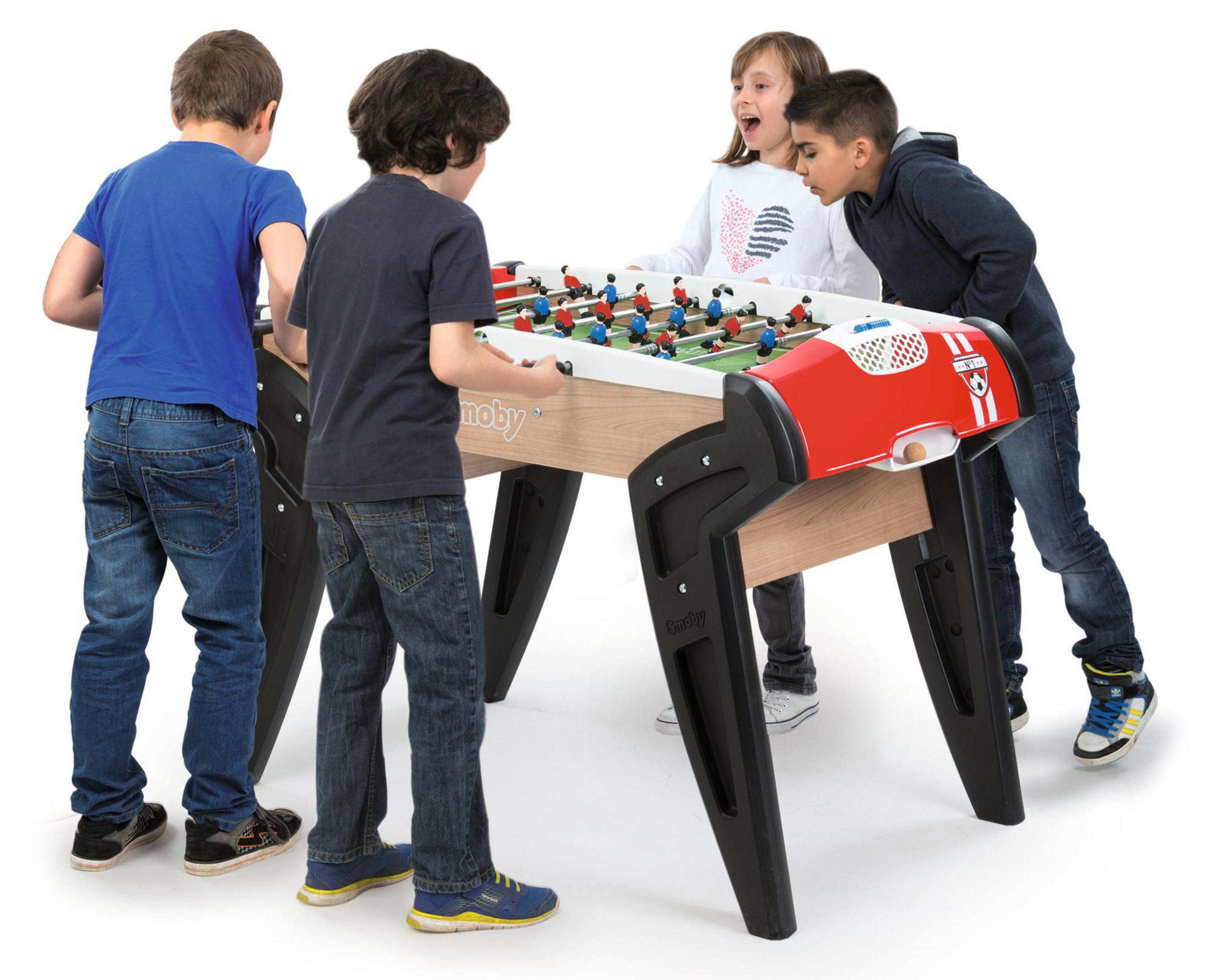 Czterech dzieci gra w piłkarzyki. Stół jest czerwono-brązowy z czarnymi nogami.