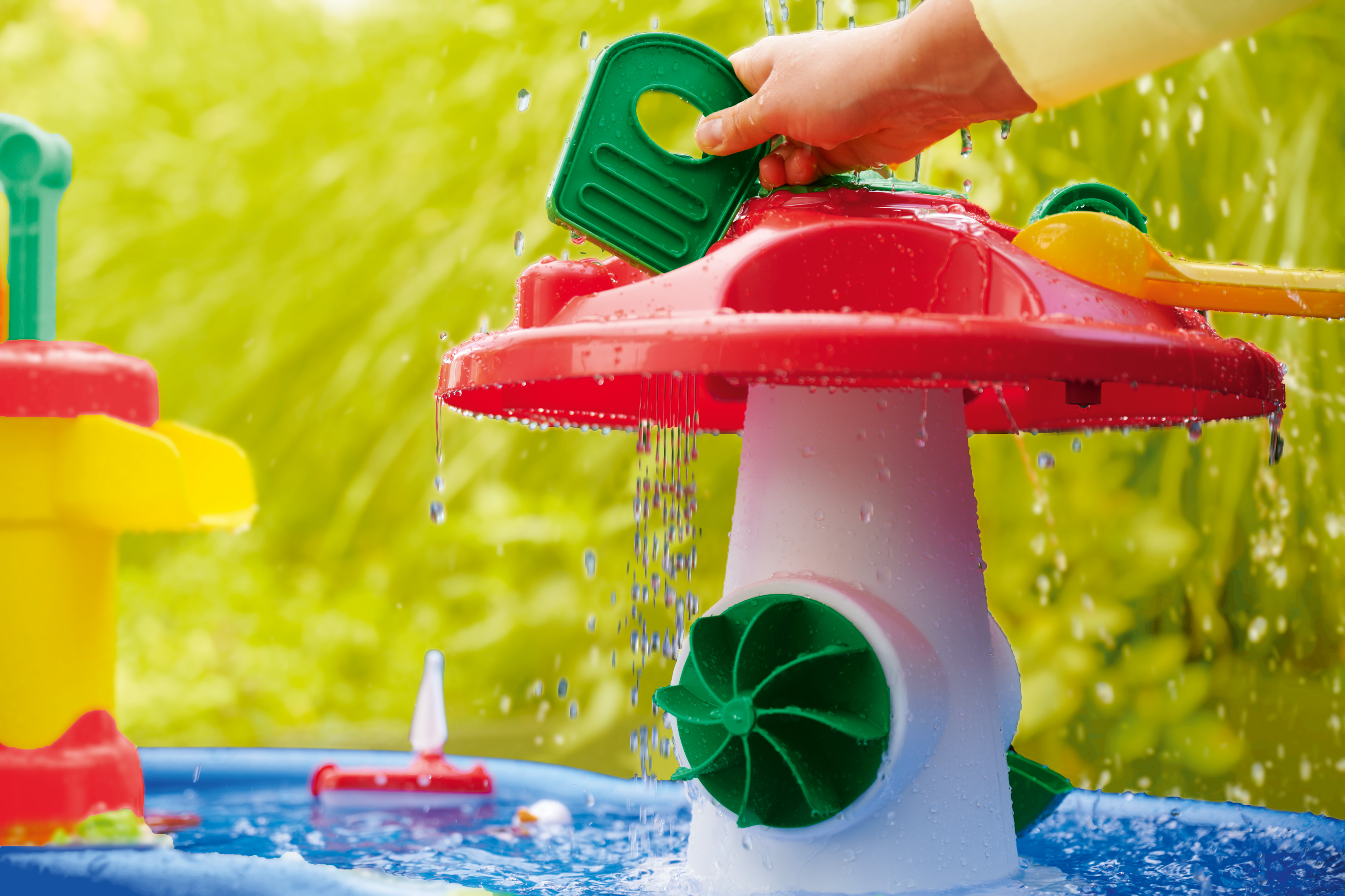 Die Hand einer Person gießt Wasser auf einen pilzförmigen Wasserspielplatz. Das Wasser fließt nach unten.