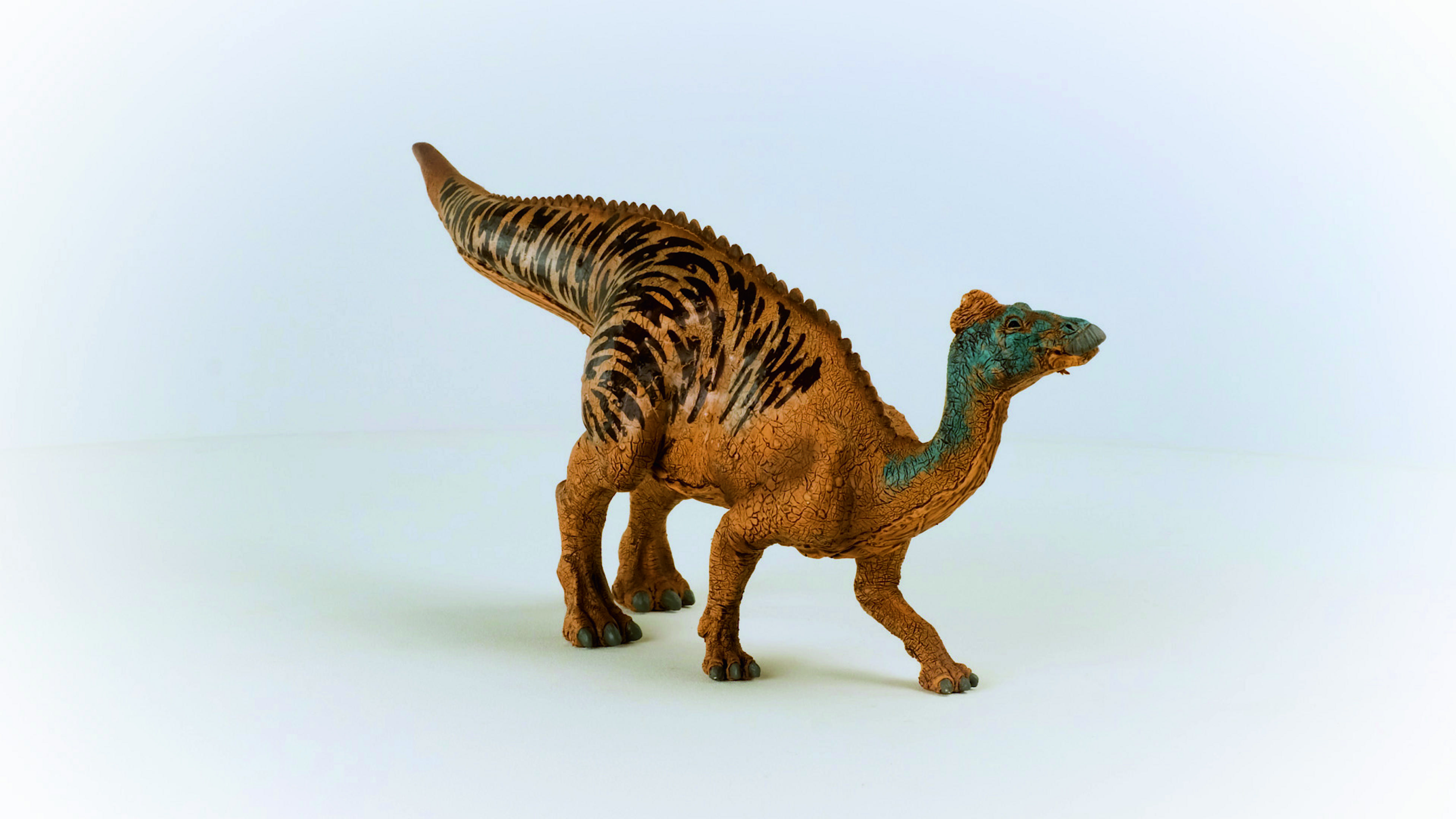 Dinosauro giocattolo, corpo marrone a strisce scure, su superficie bianca.