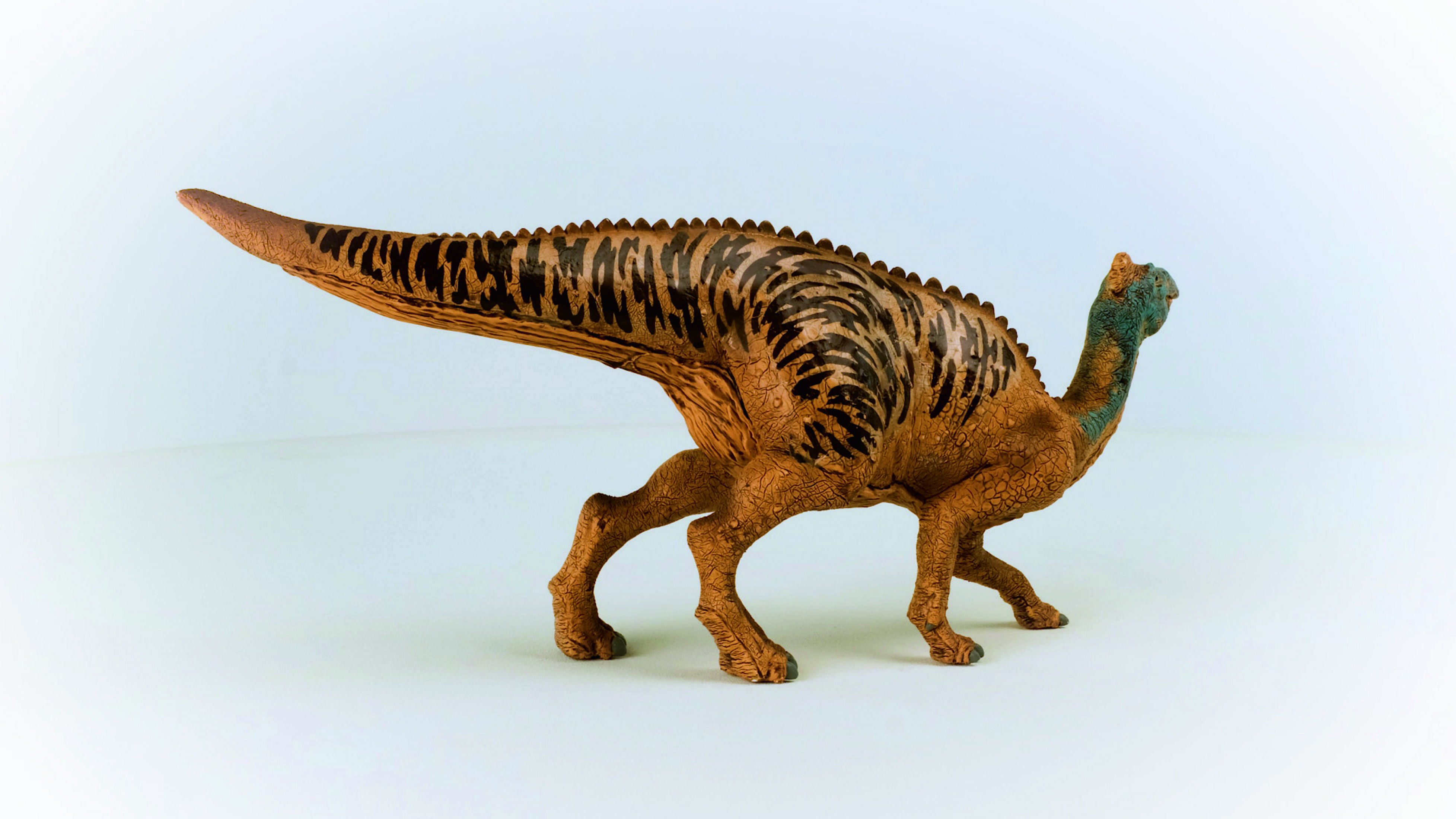 Un giocattolo a forma di dinosauro marrone e beige con coda lunga su sfondo bianco.