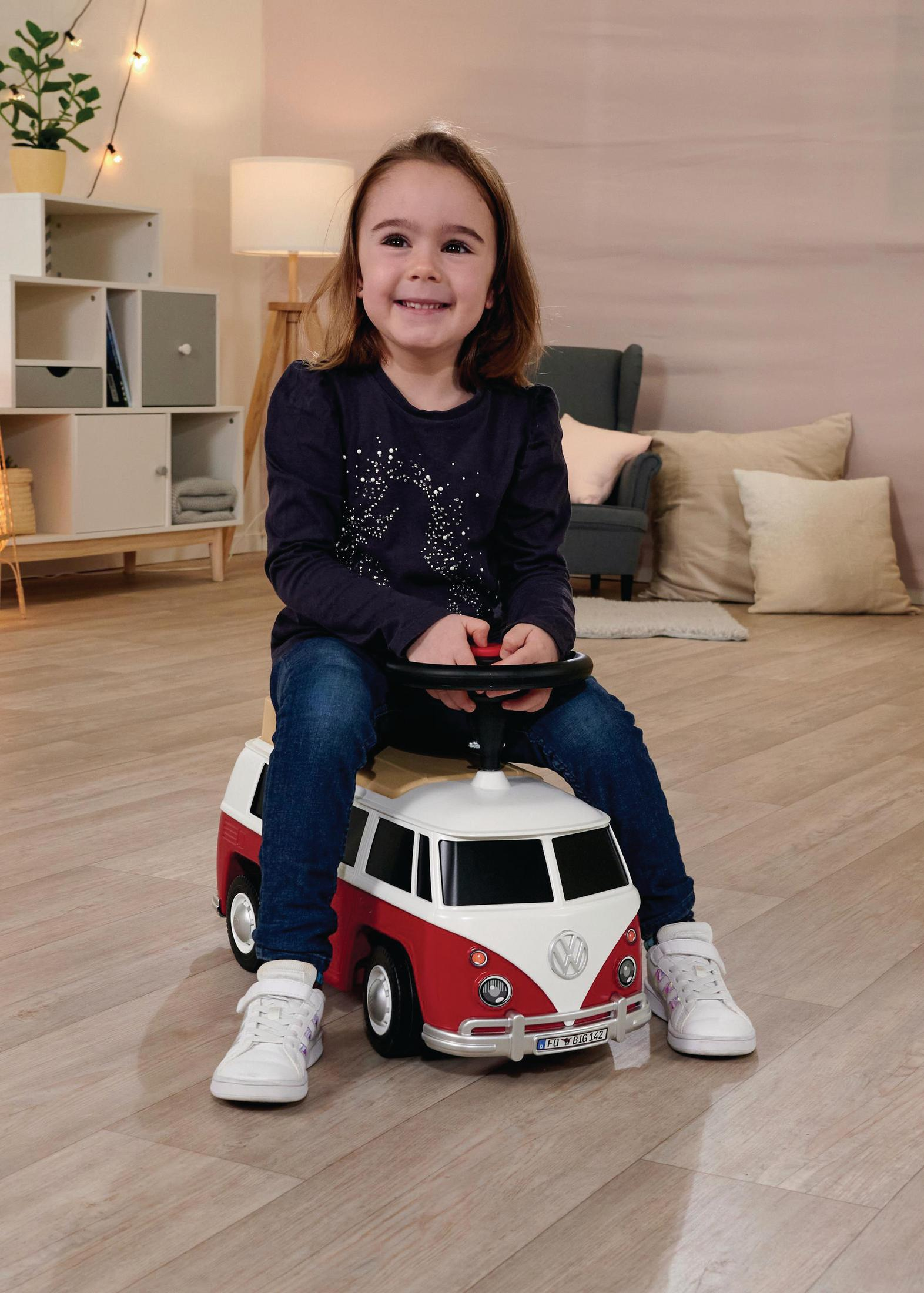 Ein junges Mädchen lächelt, während es in einem rot-weißen Spielzeugauto sitzt, in einer Heimatumgebung.