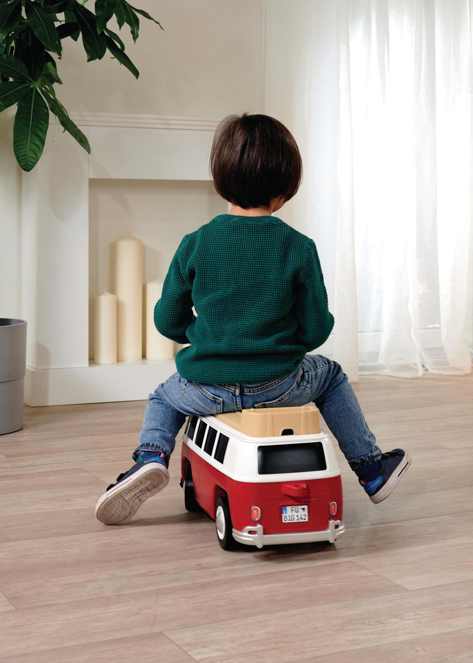 Ein Kind sitzt auf einem roten und weißen VW-Camper-Van-Spielzeug. Das Kind ist von der Kamera abgewandt.