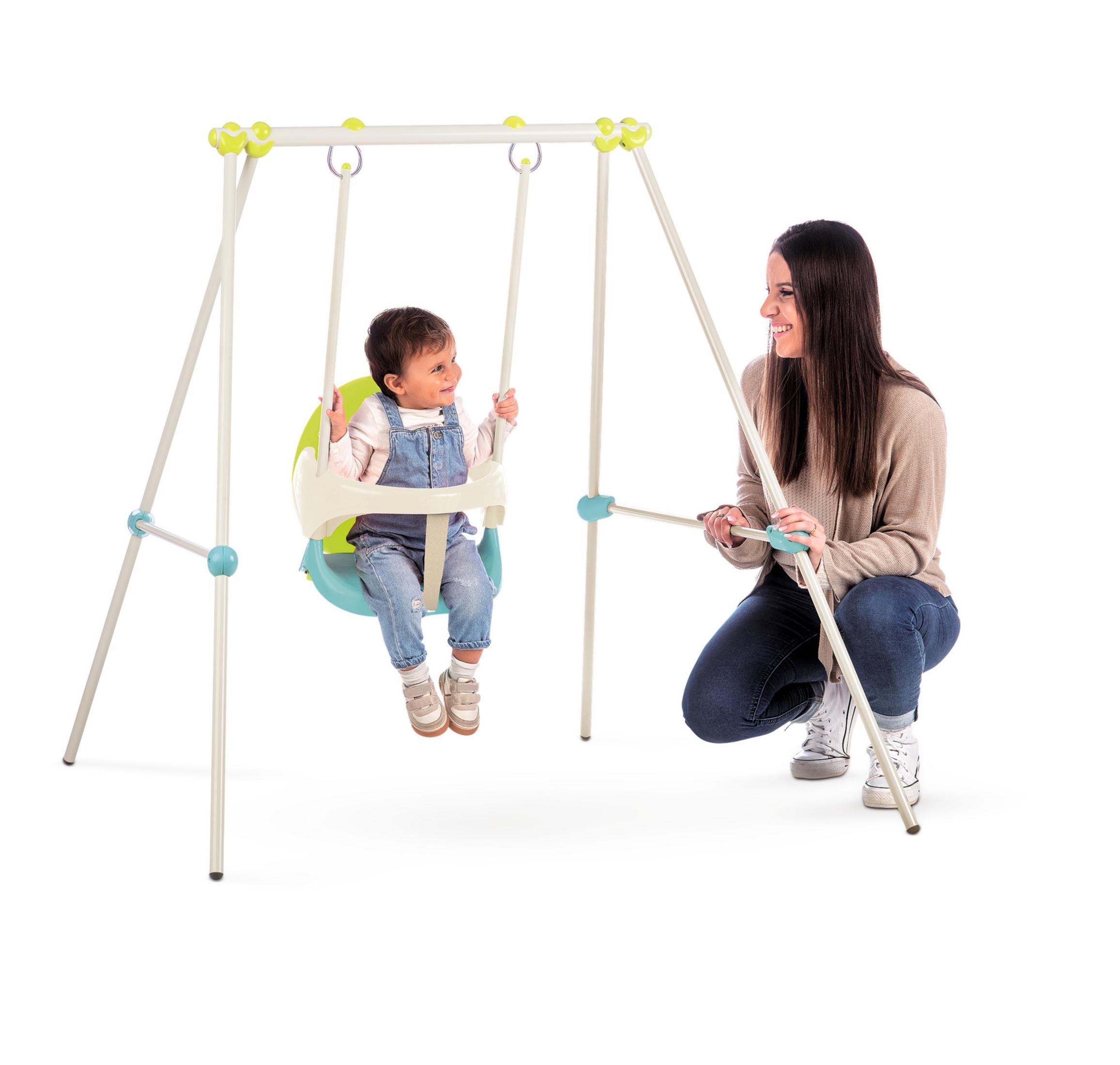 Ein Schaukelgerüst mit einem Baby in der Schaukel. Eine Frau steht und hilft dem Baby. Weißer Hintergrund.