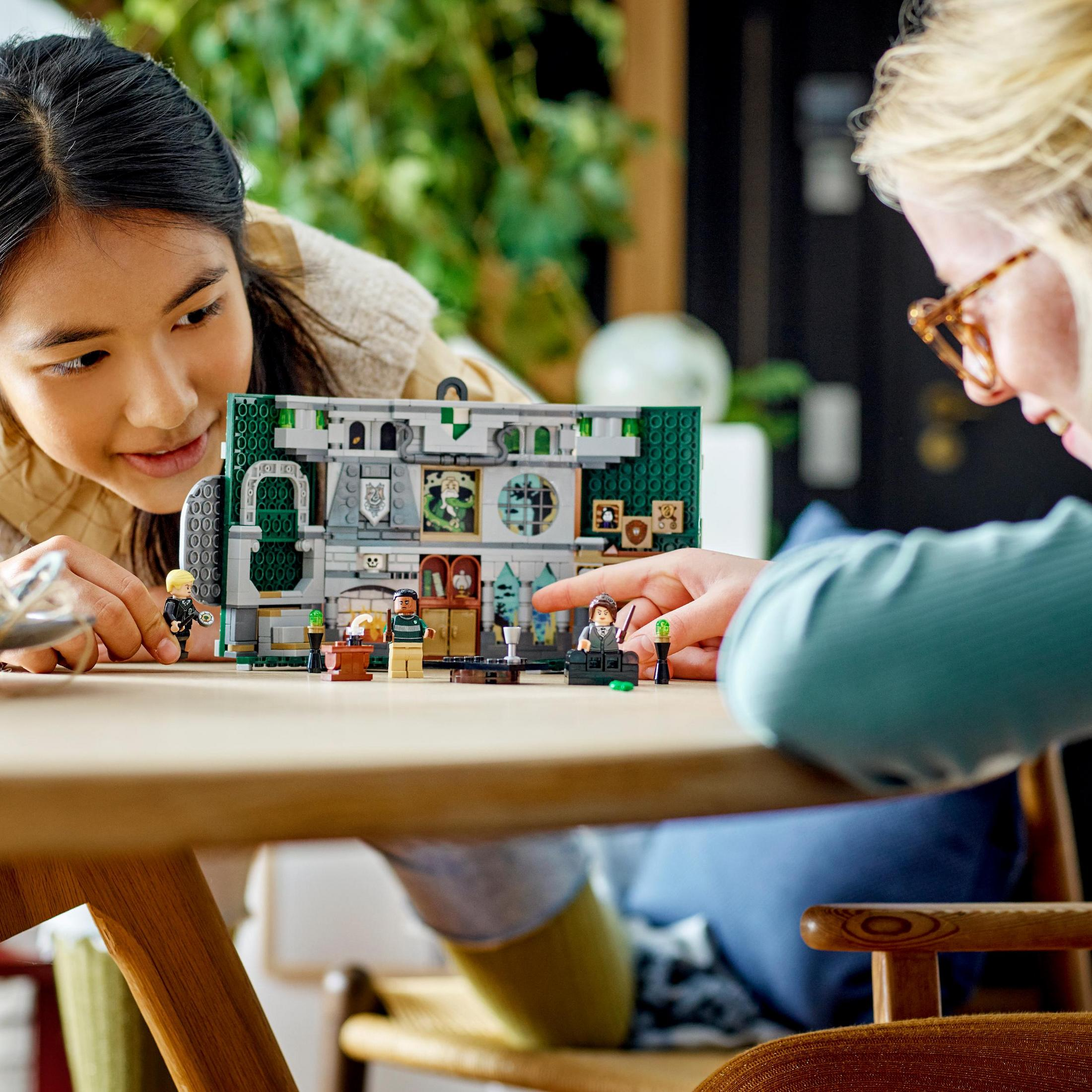 Zwei Personen spielen mit einem Lego-Set. Ein Modell eines Gebäudes steht auf dem Tisch.