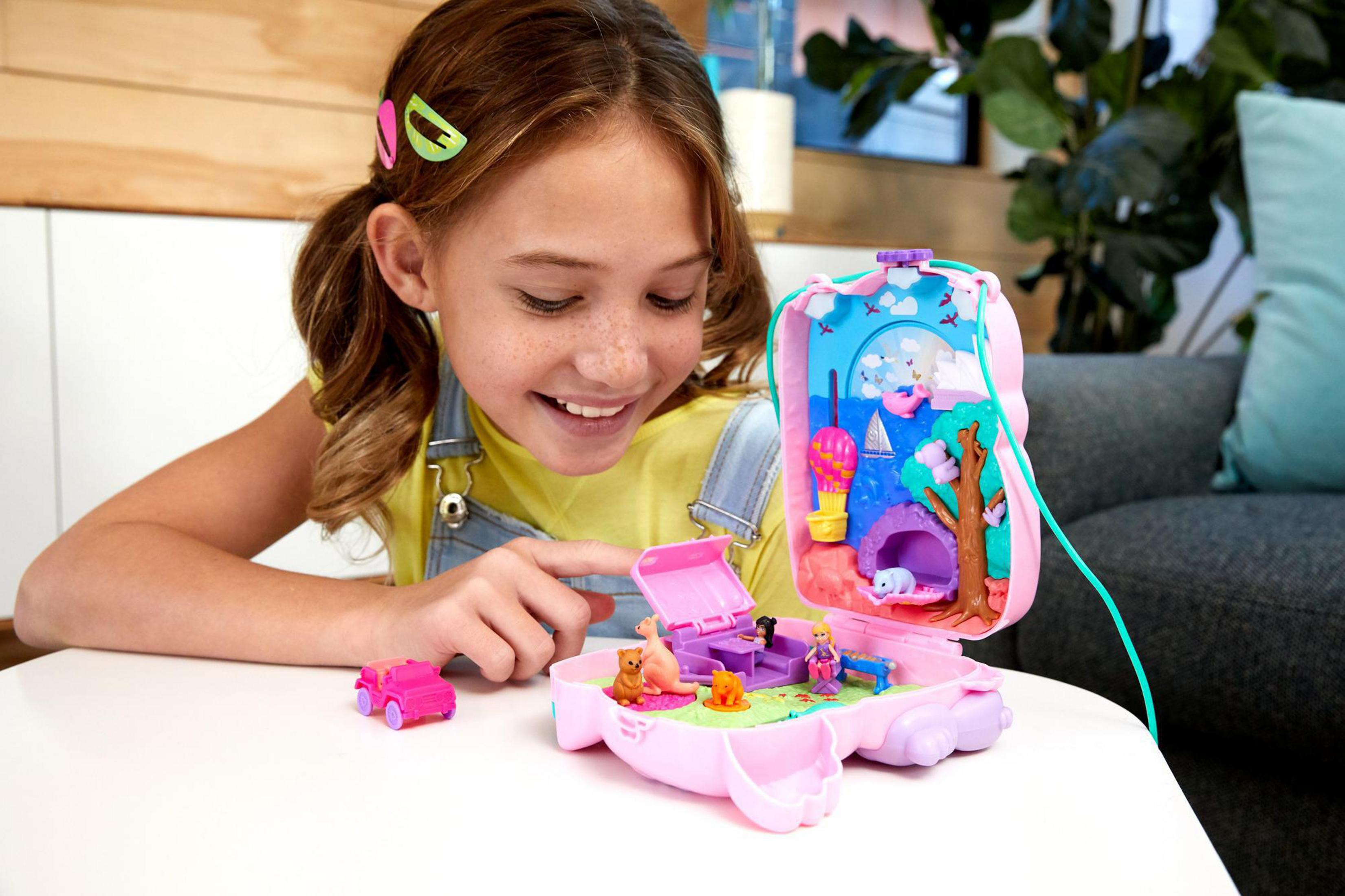 Ein Mädchen spielt mit einem pinkfarbenen Polly Pocket Set. Es hat ein kleines Auto, Tiere und ein Miniaturhaus.