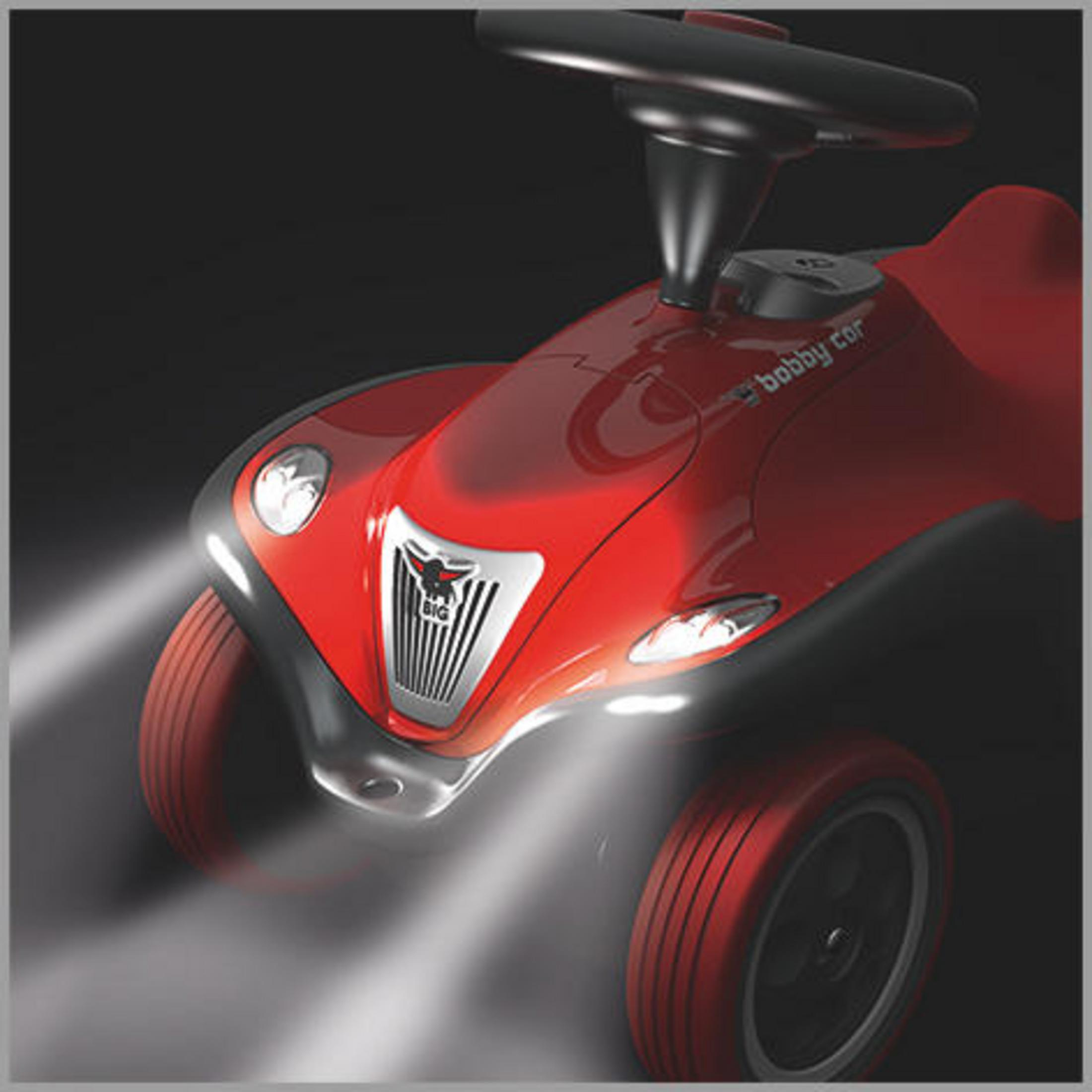 Ein rotes Spielzeugauto mit schwarzem Lenkrad und Scheinwerfern auf dunklem Hintergrund.