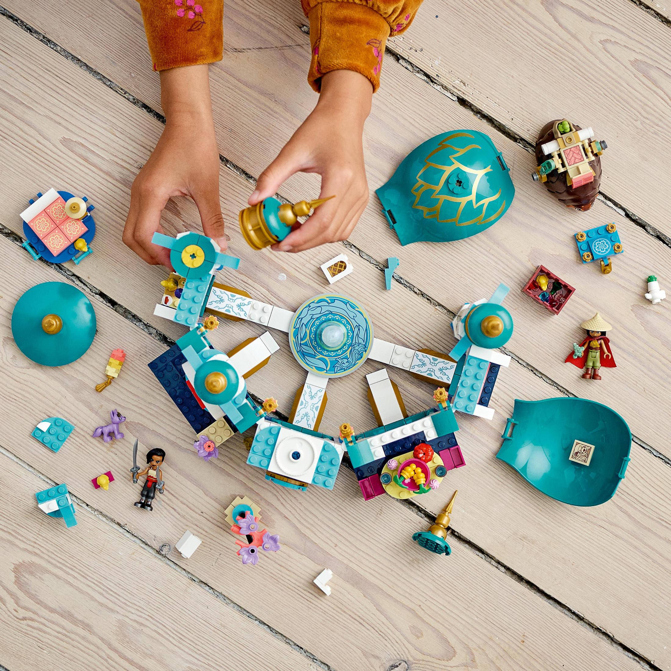 Dziecko składa klocki Lego. Różne części Lego są rozrzucone na drewnianej powierzchni.
