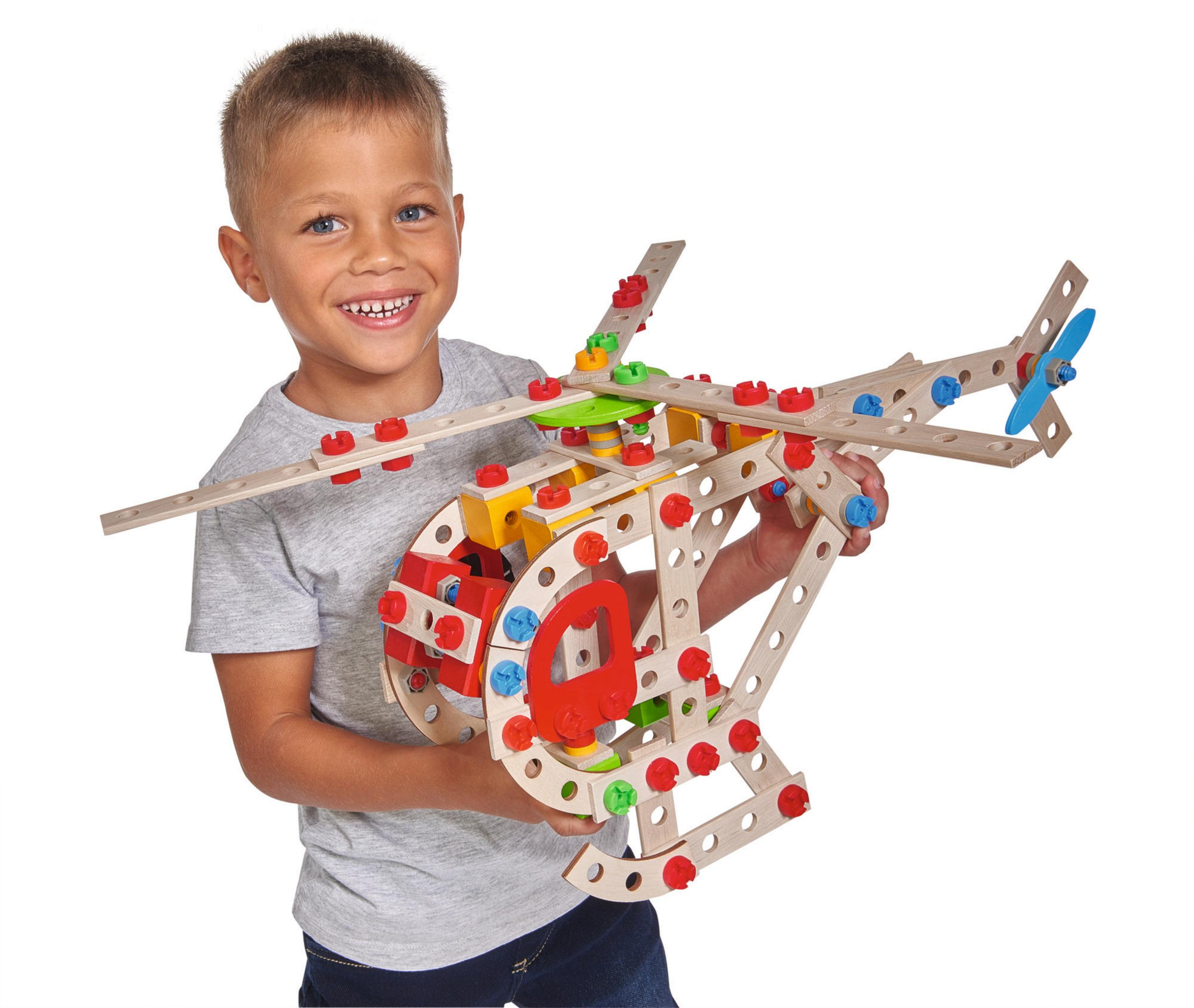 Ein Junge hält ein Holz-Helikopter-Spielzeug mit breitem Lächeln auf weißem Hintergrund.