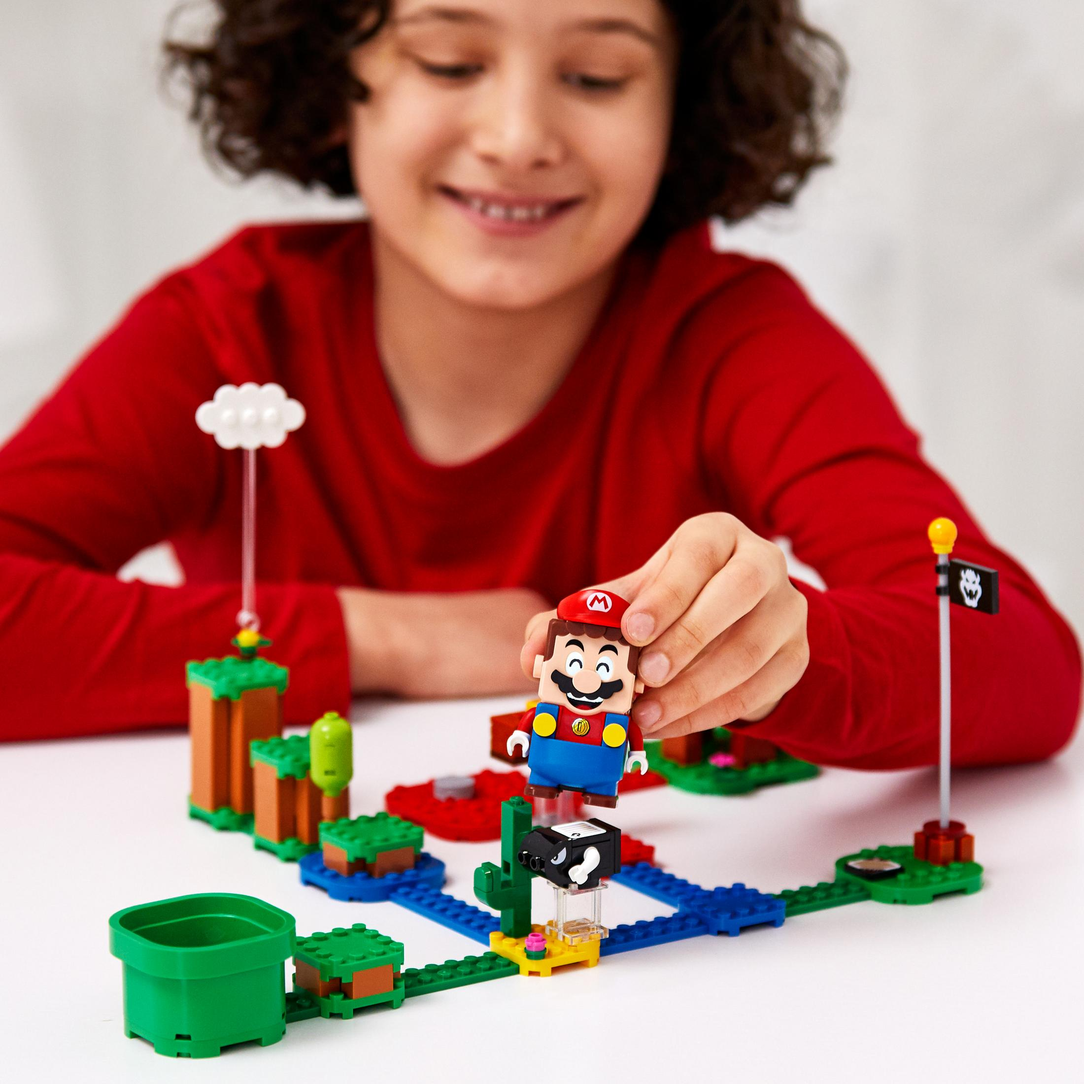 Un bambino sorride, gioca con Lego Mario e un mondo Lego.