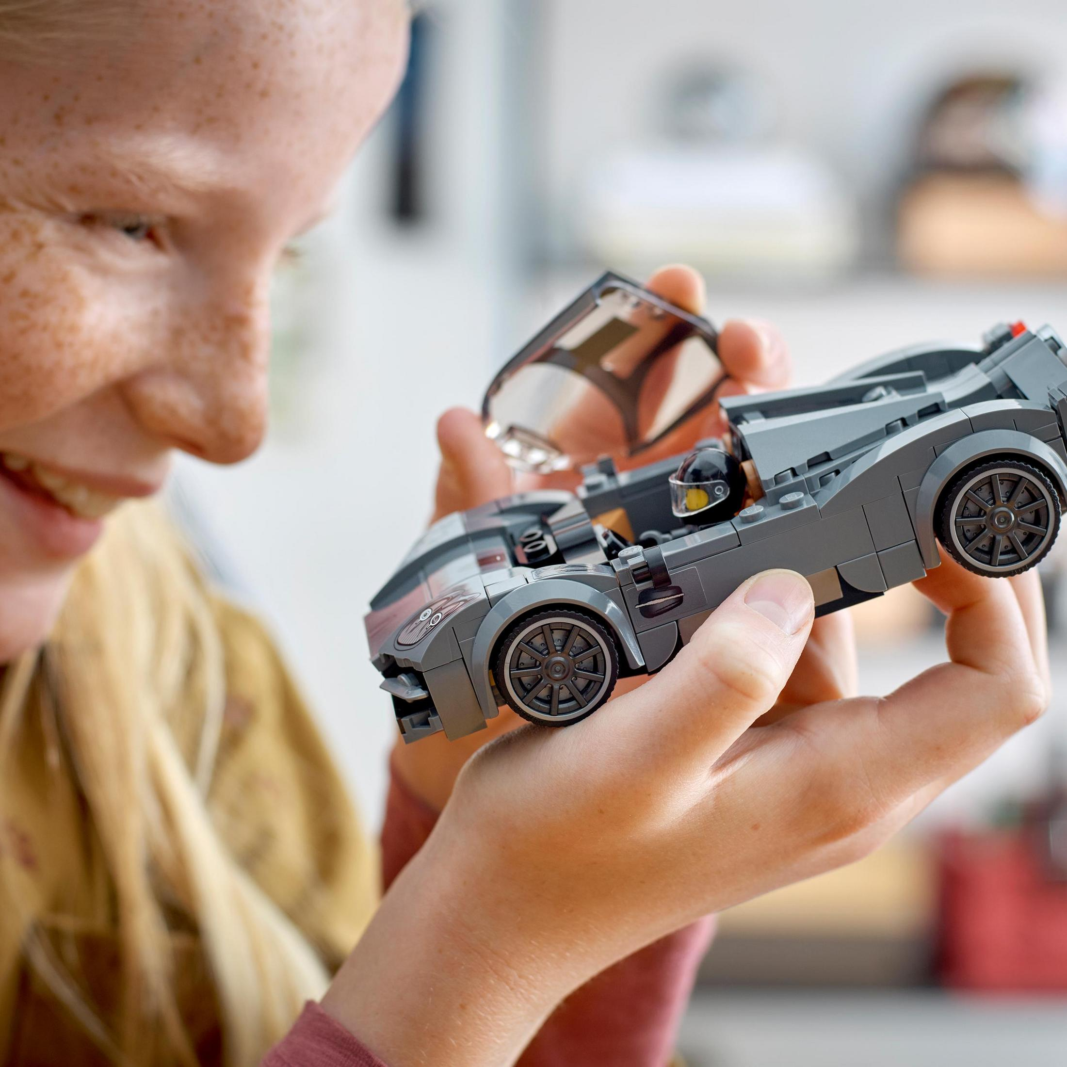 Une personne tient une voiture Lego et sourit. Une pièce transparente est devant la voiture.