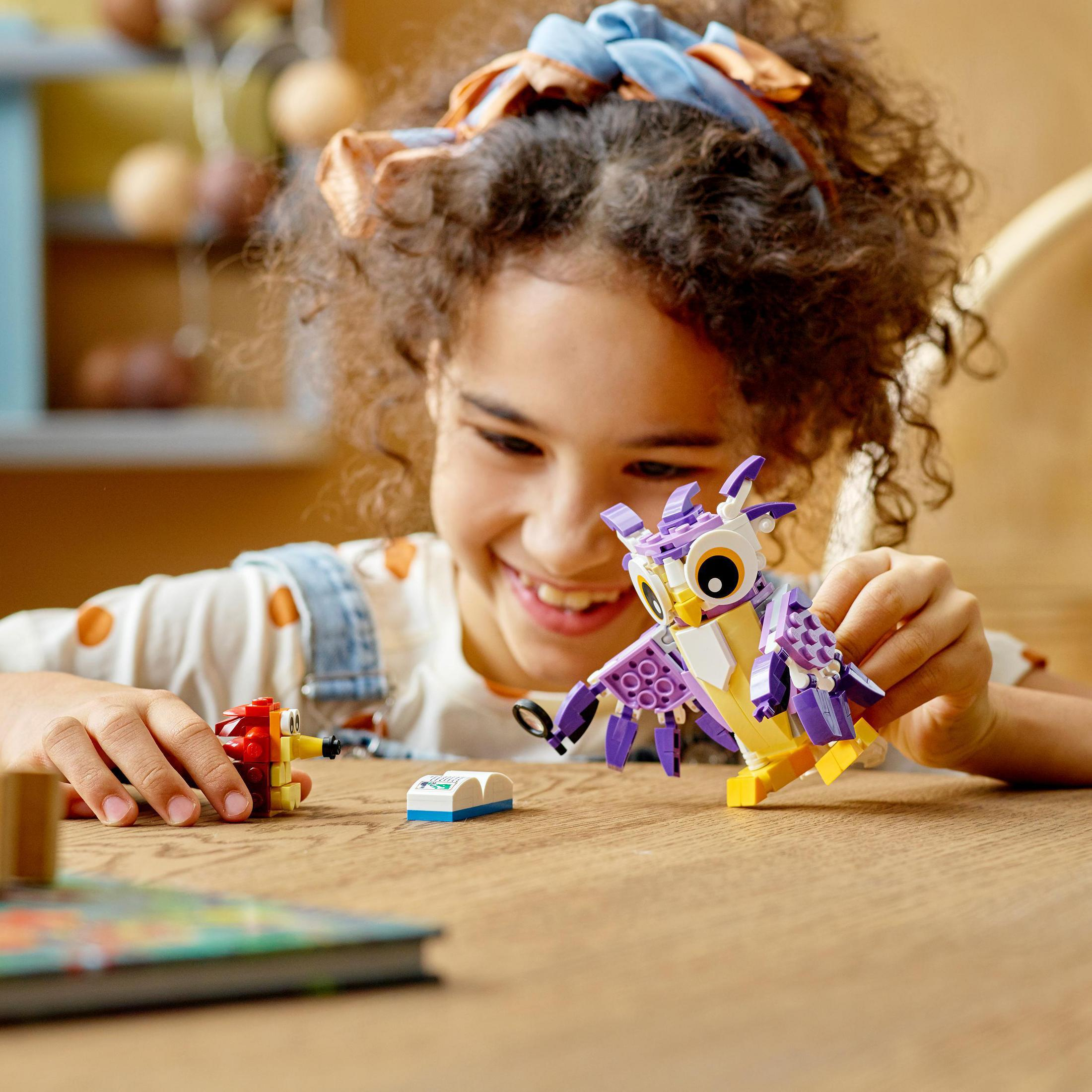 Niña jugando con un búho Lego. Hay bloques de Lego en la mesa de madera. Rostro sonriente.