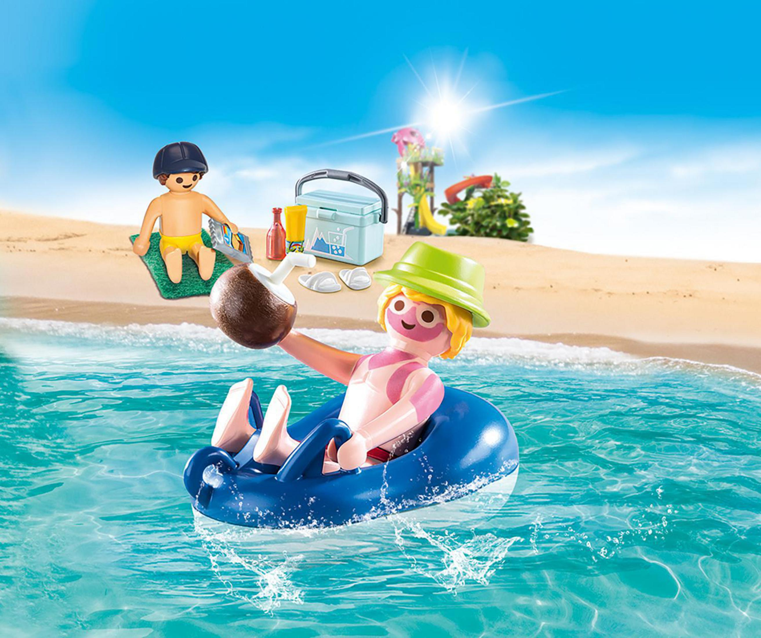 Playmobil-Figuren in einer Strandszene: eine Person auf einer Tube, eine andere auf einem Handtuch und eine Kühlbox.