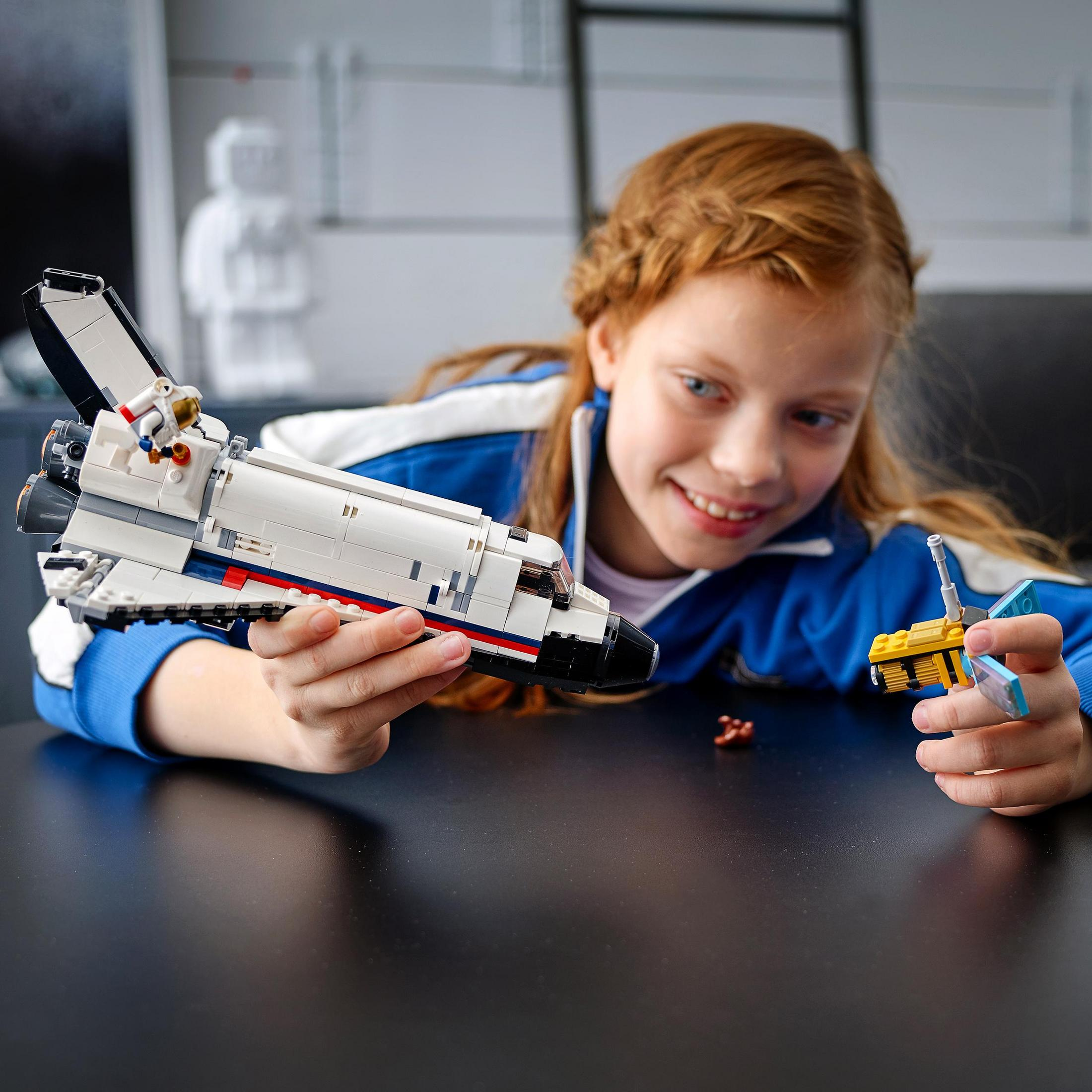 Ein Mädchen lächelt und hält ein weiß-schwarzes Spielzeug-Space Shuttle und ein gelbes Spielzeug.