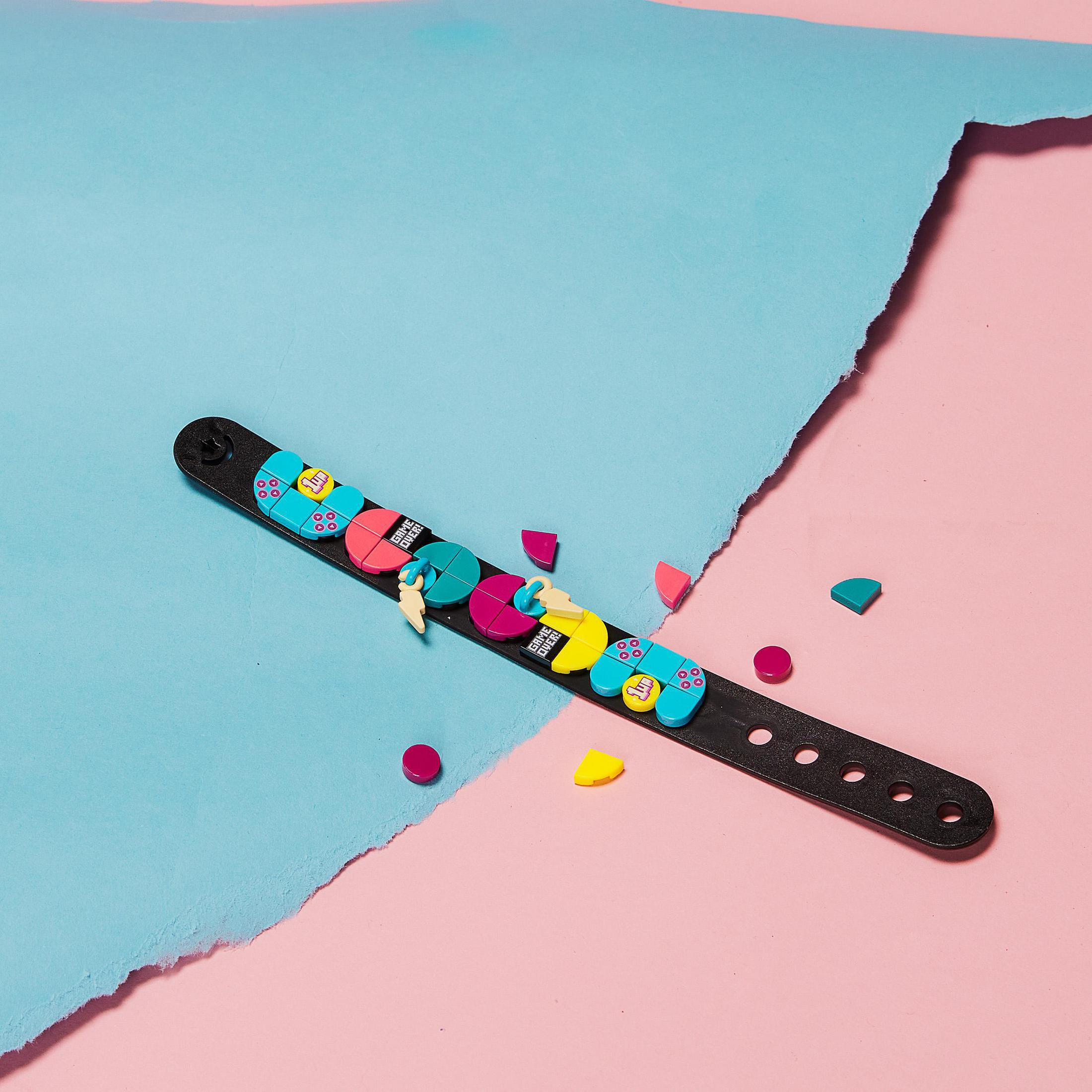 Ein LEGO Dots Armband mit bunten Kacheln, verstreut auf einer rosa und blauen Oberfläche.