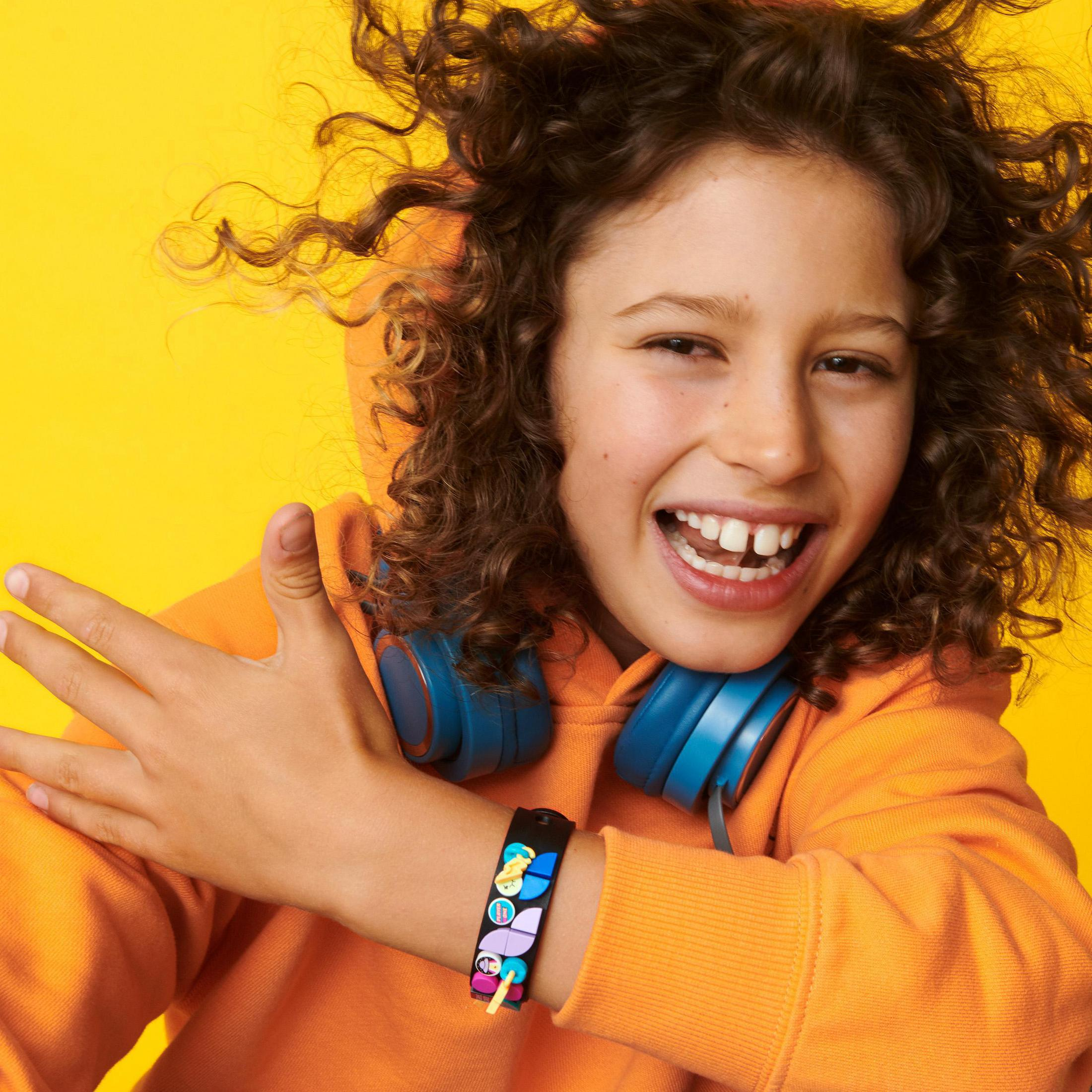 Ein lächelndes Kind trägt Kopfhörer um den Hals und ein Armband mit Zeichentrickfiguren.