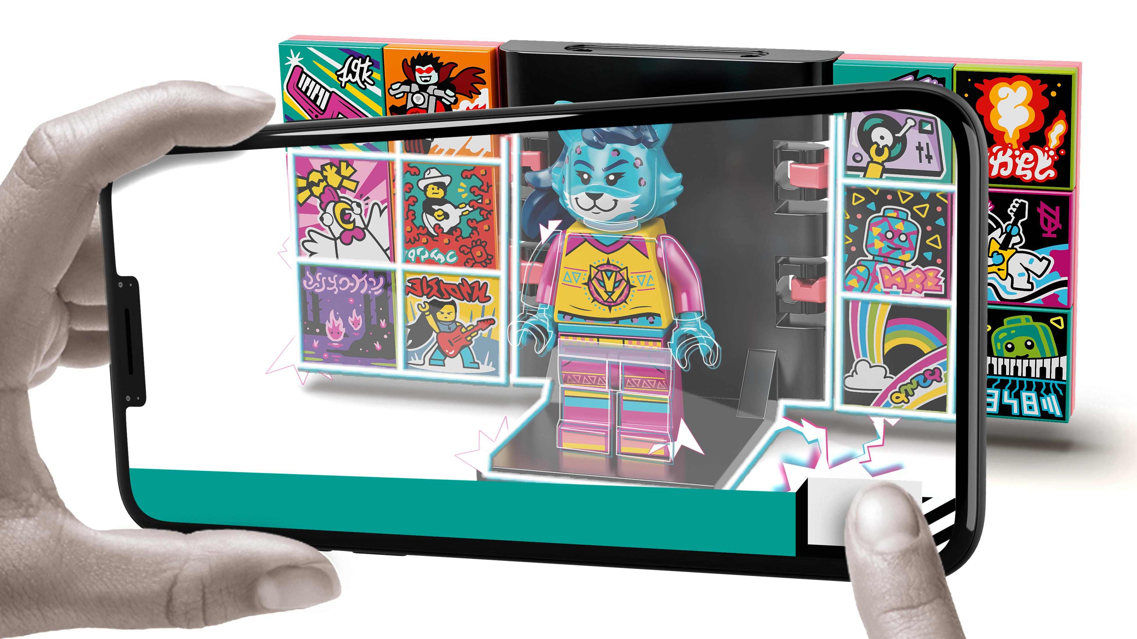 Ręka trzymająca telefon z figurką LEGO. W tle inne pudełka LEGO.