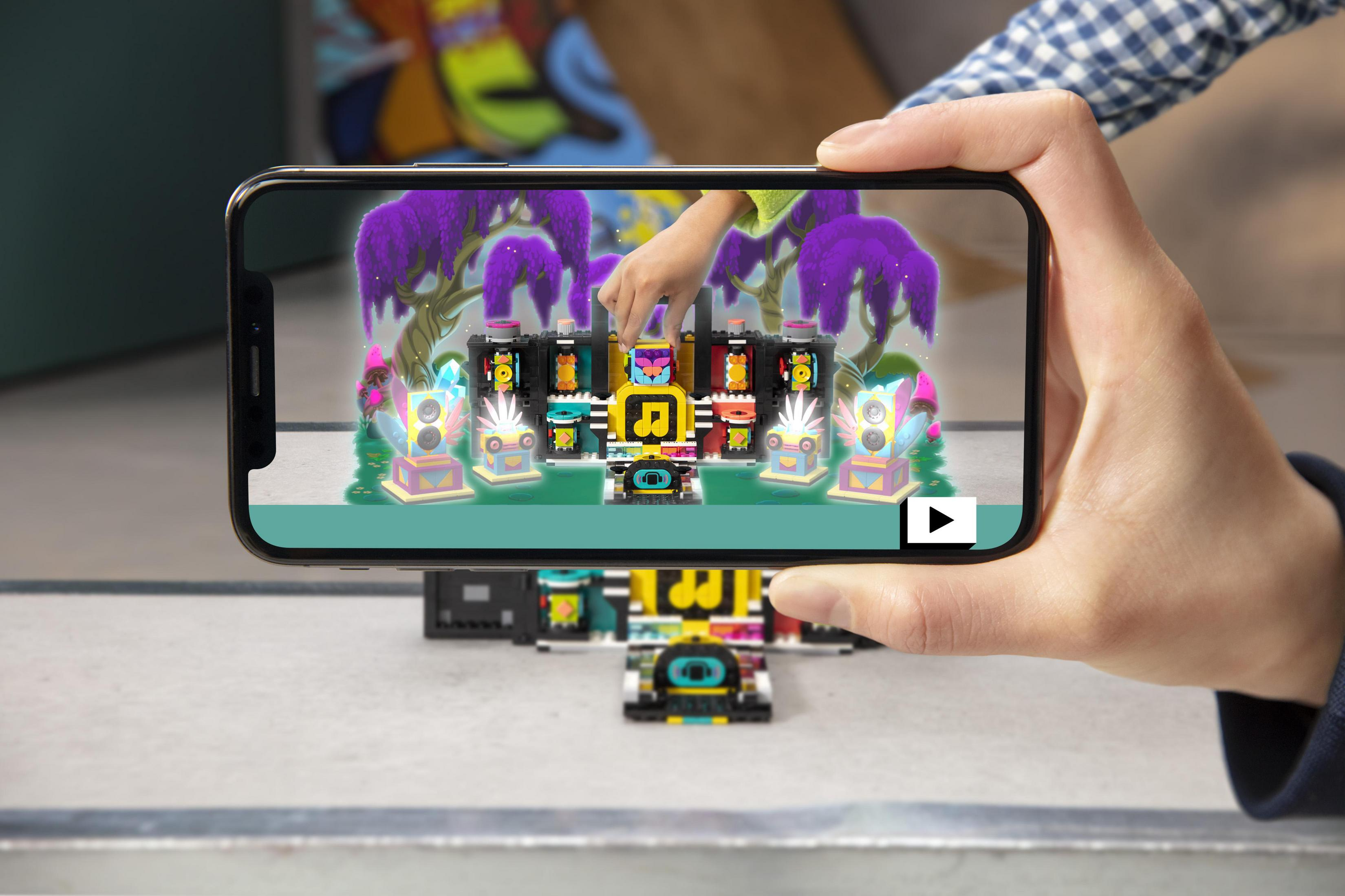 Dłoń trzymająca telefon wyświetla zestaw Lego z głośnikami i nutami muzycznymi.