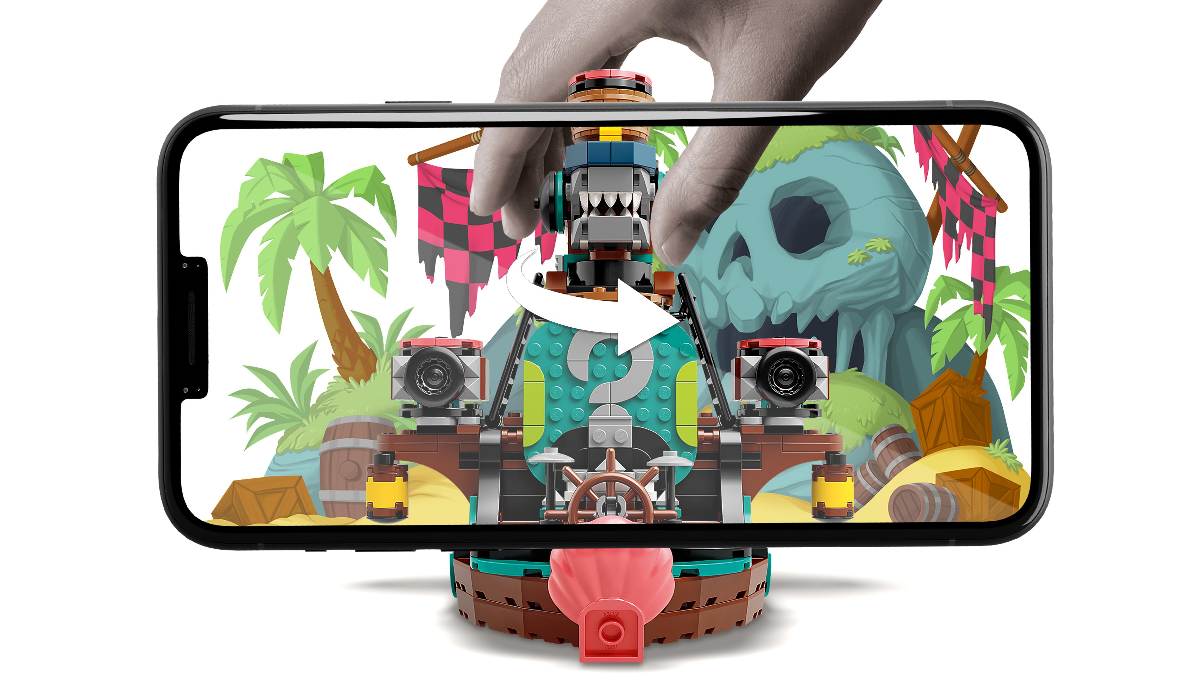 Dłoń trzyma telefon z zabawką pirackiego statku z palmami i czaszką.