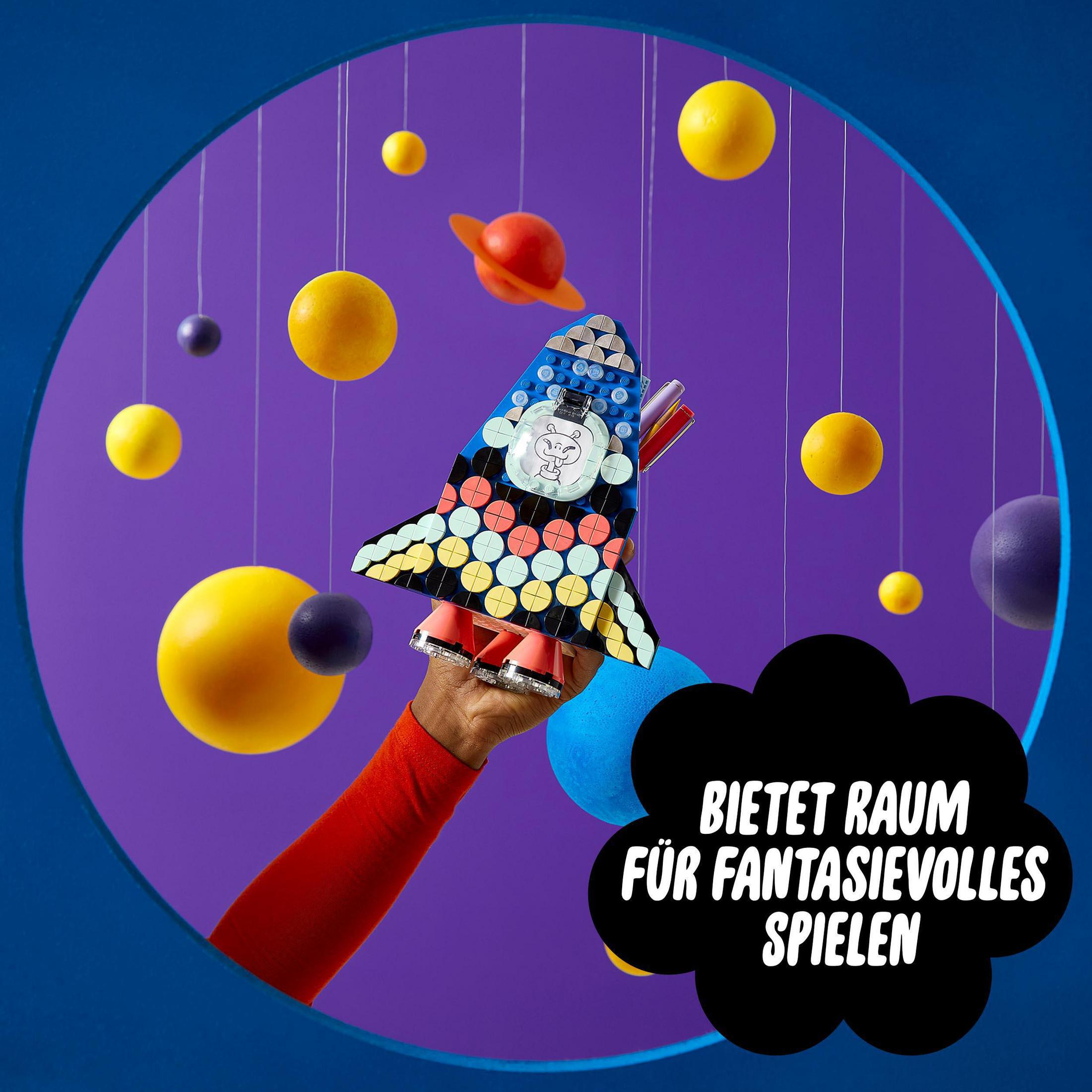 Eine Spielzeugrakete in der Hand mit Planeten und lila Hintergrund. Text: 