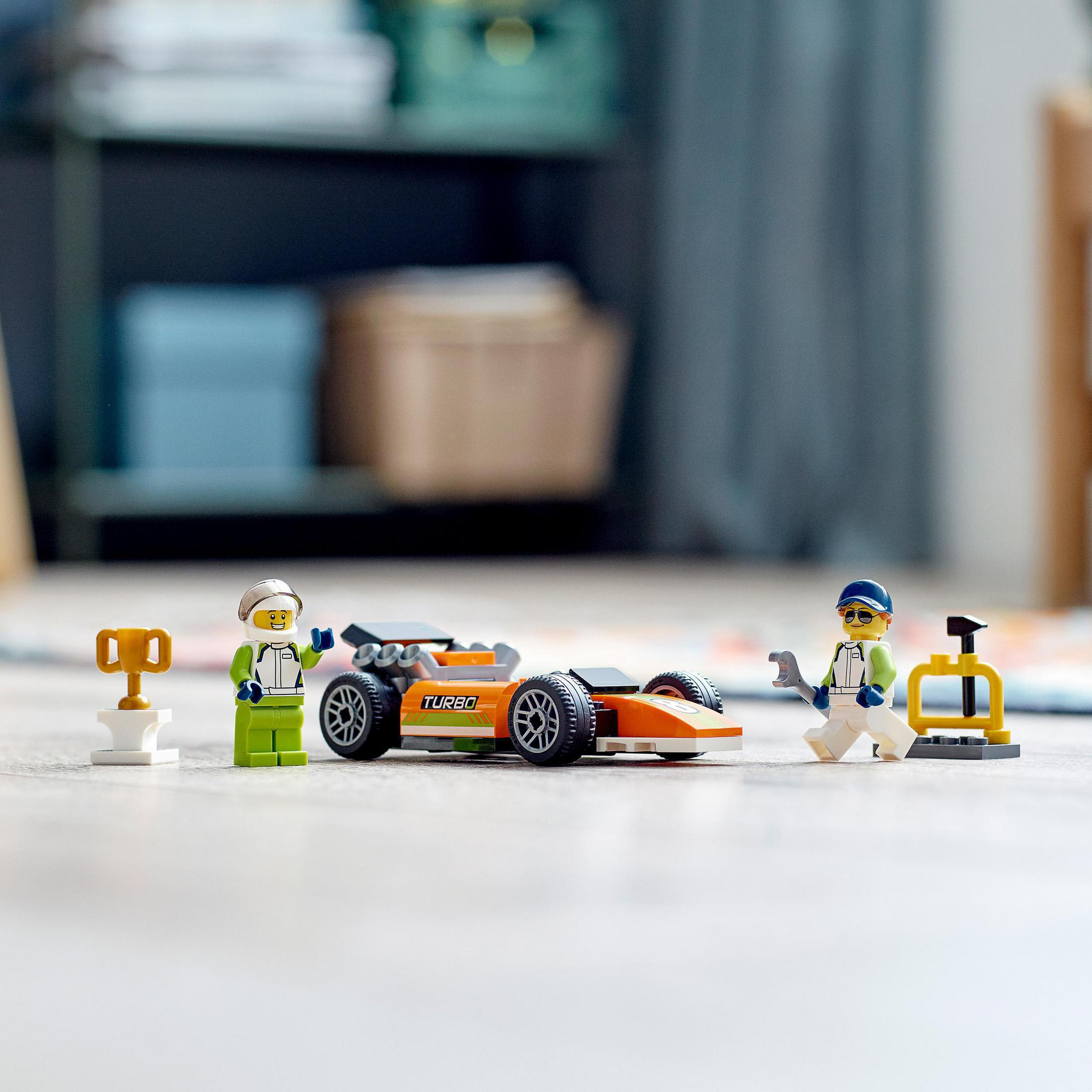 Lego raceauto set met twee figuren, een trofee en gereedschap. De auto is oranje en zwart.
