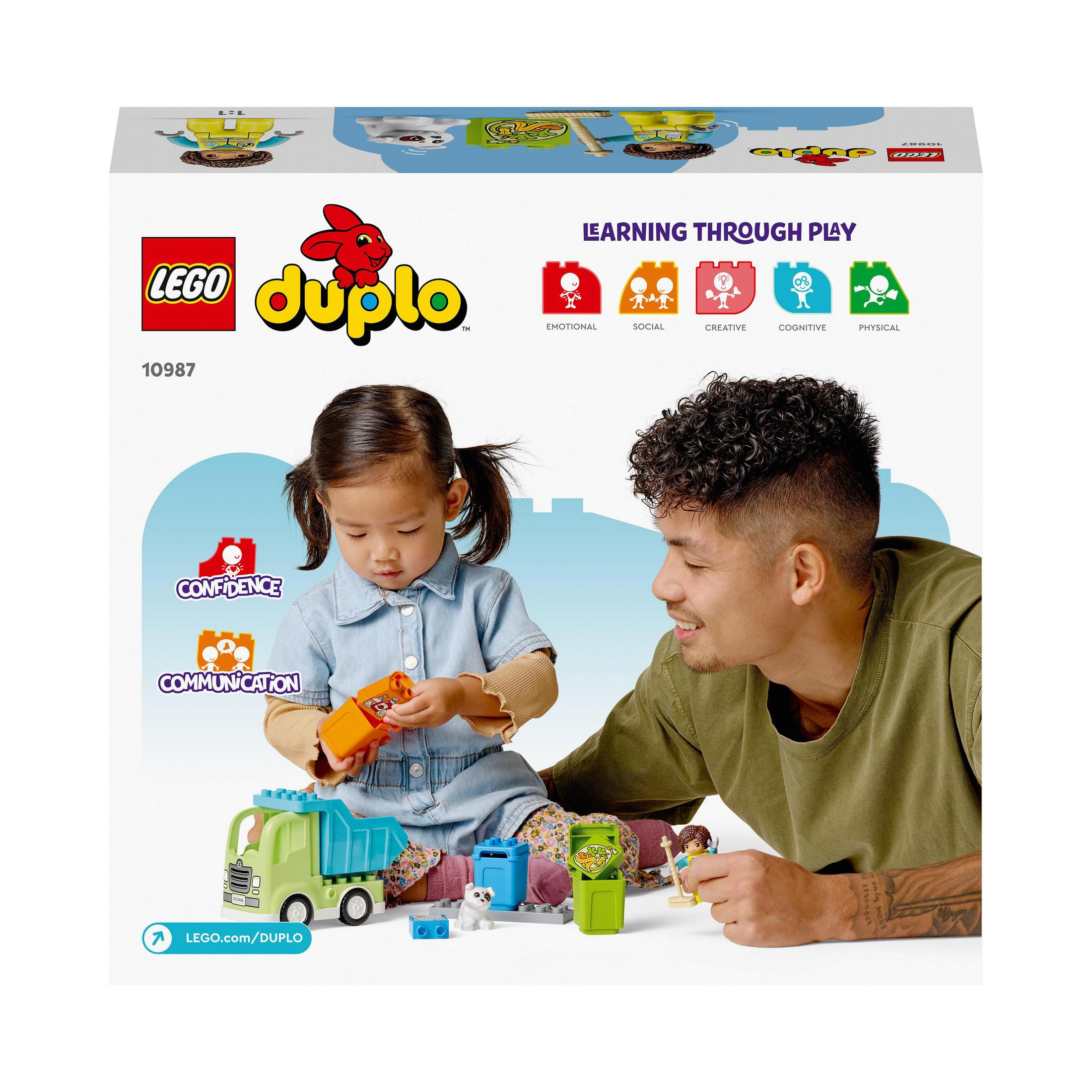 Ein Mädchen und ein Mann spielen mit Lego Duplo Blöcken. Ein LKW, Mülltonnen und Blöcke liegen auf dem Boden.