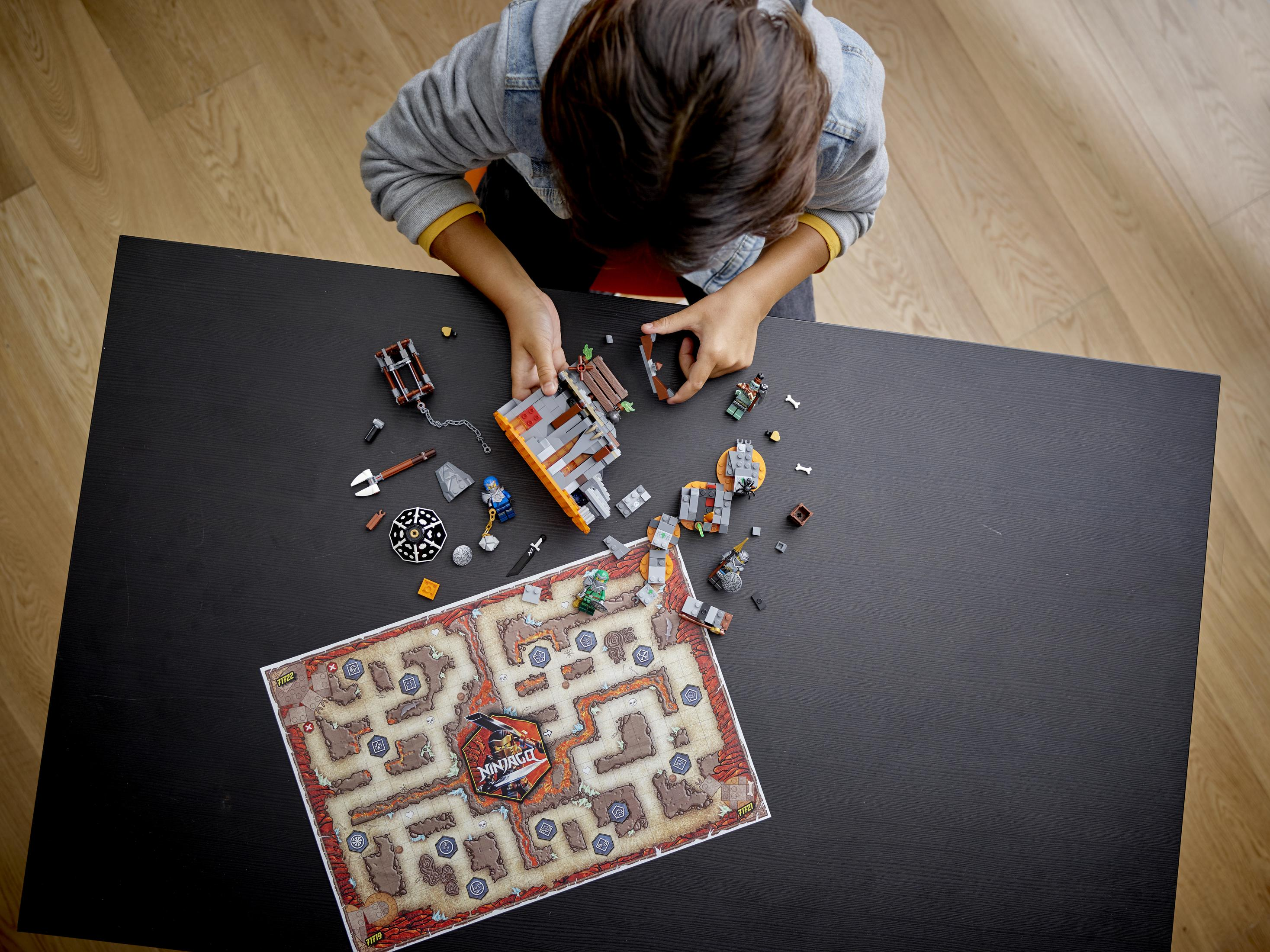 Ein Kind spielt mit LEGO-Steinen auf einem schwarzen Tisch. Eine Karte und LEGO-Strukturen sind vorhanden.