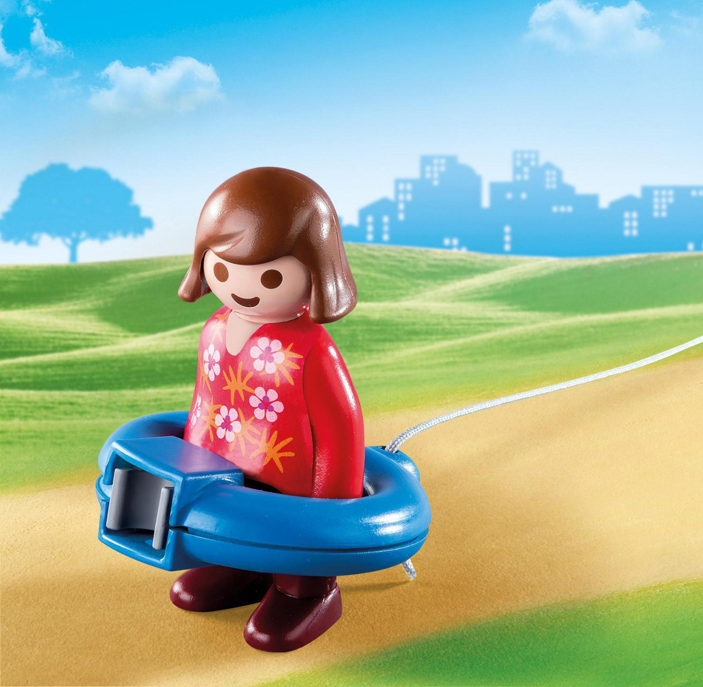 Playmobil-Mädchen mit blauem Ring und Schnur. Hintergrund: grüne Wiese und blauer Himmel.