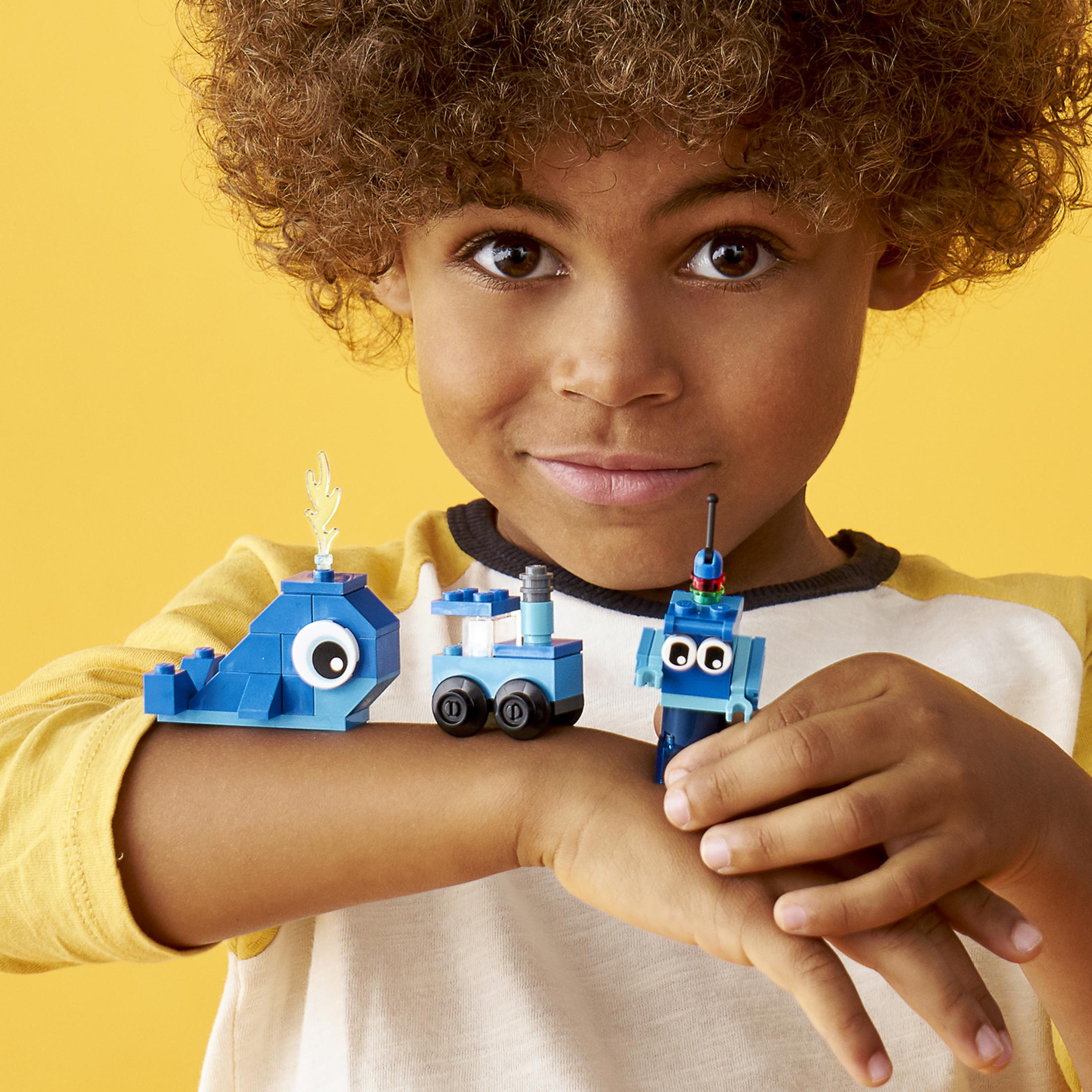 Ein Junge hält drei kleine Lego-Kreationen: einen blauen Wal, einen Zug und einen Roboter.