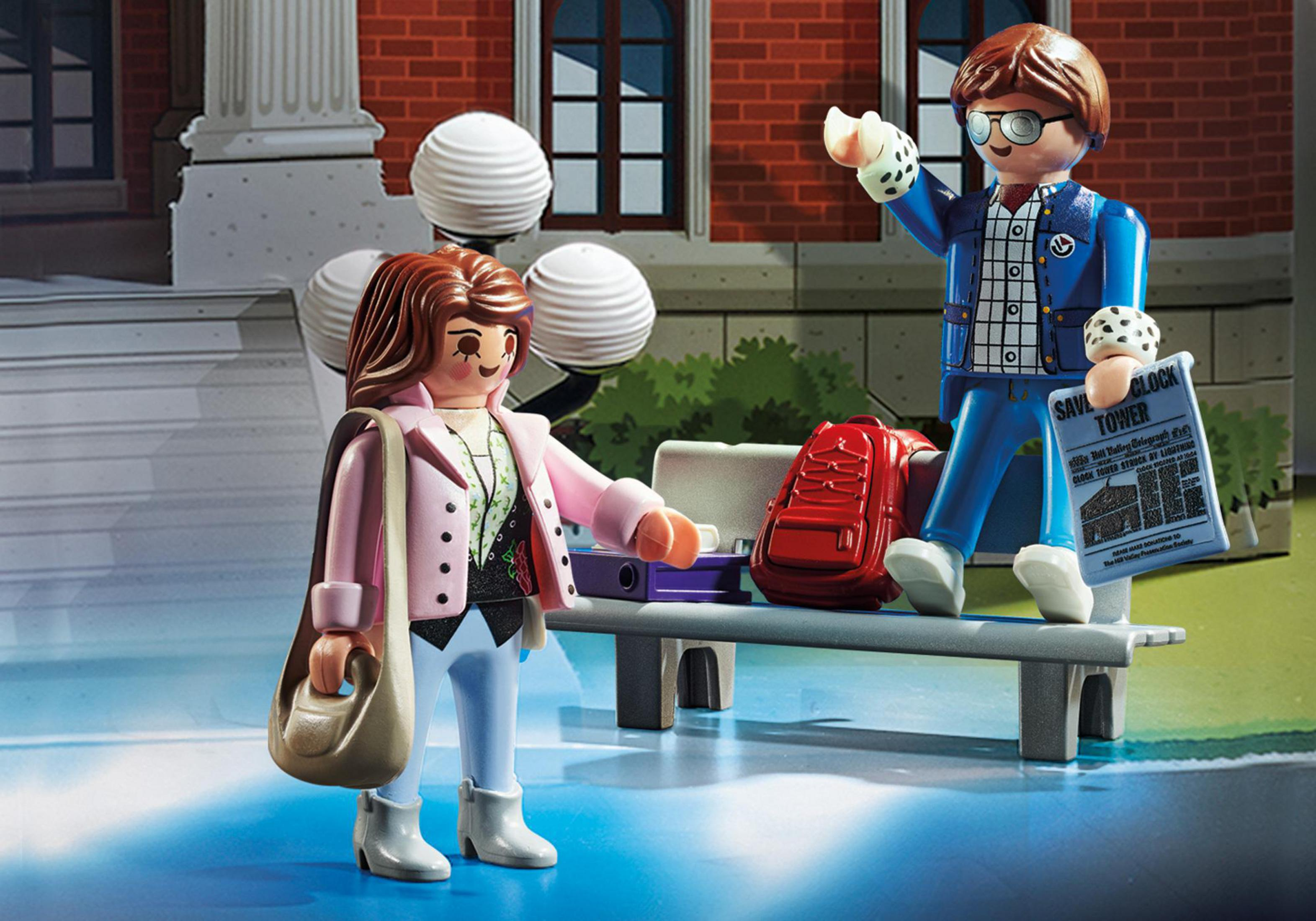 Playmobil-Set mit Figuren in einer Schulszene. Eine Figur winkt. Schulgebäude im Hintergrund.