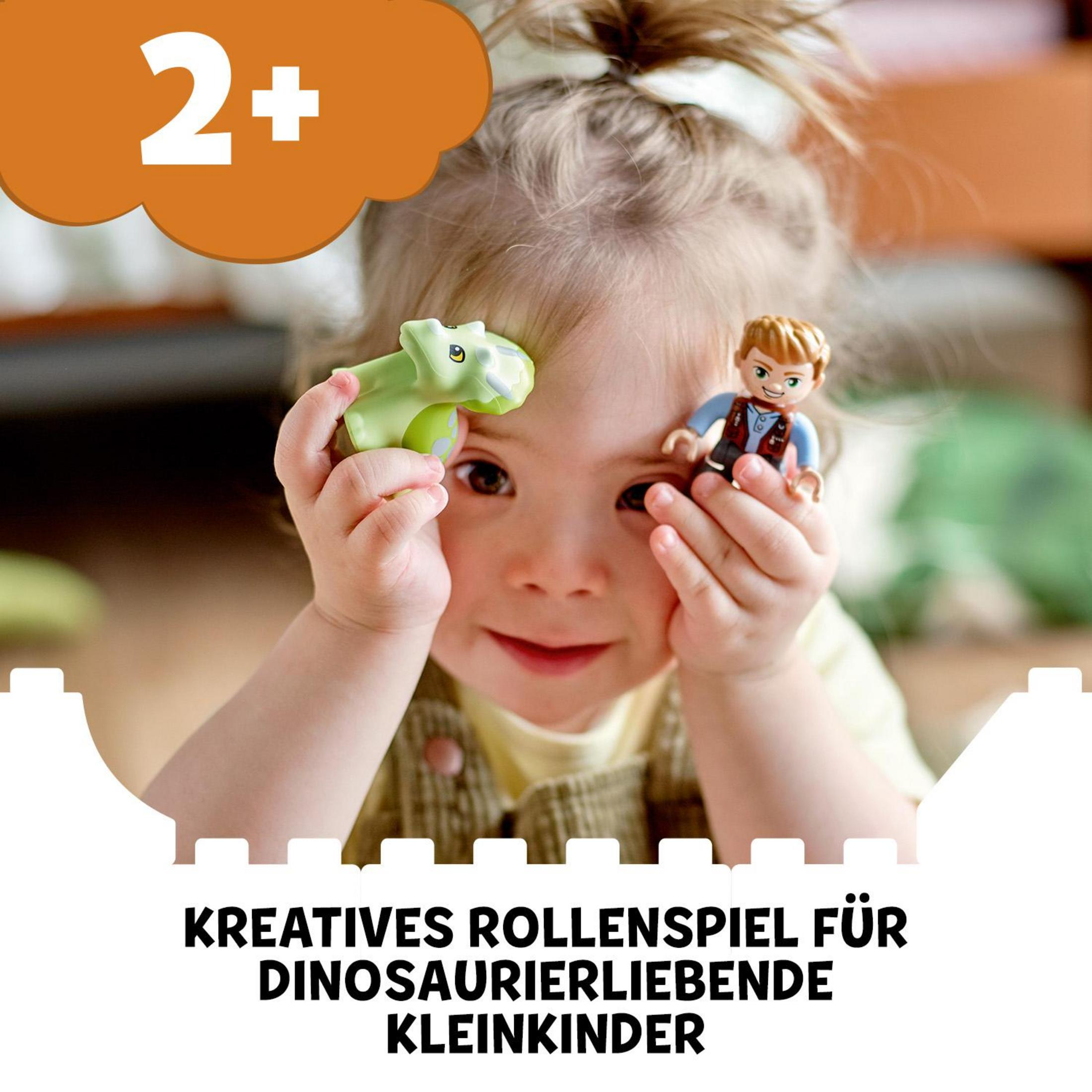 Un bambino che tiene un giocattolo dinosauro verde, con un ragazzo e testo in tedesco.