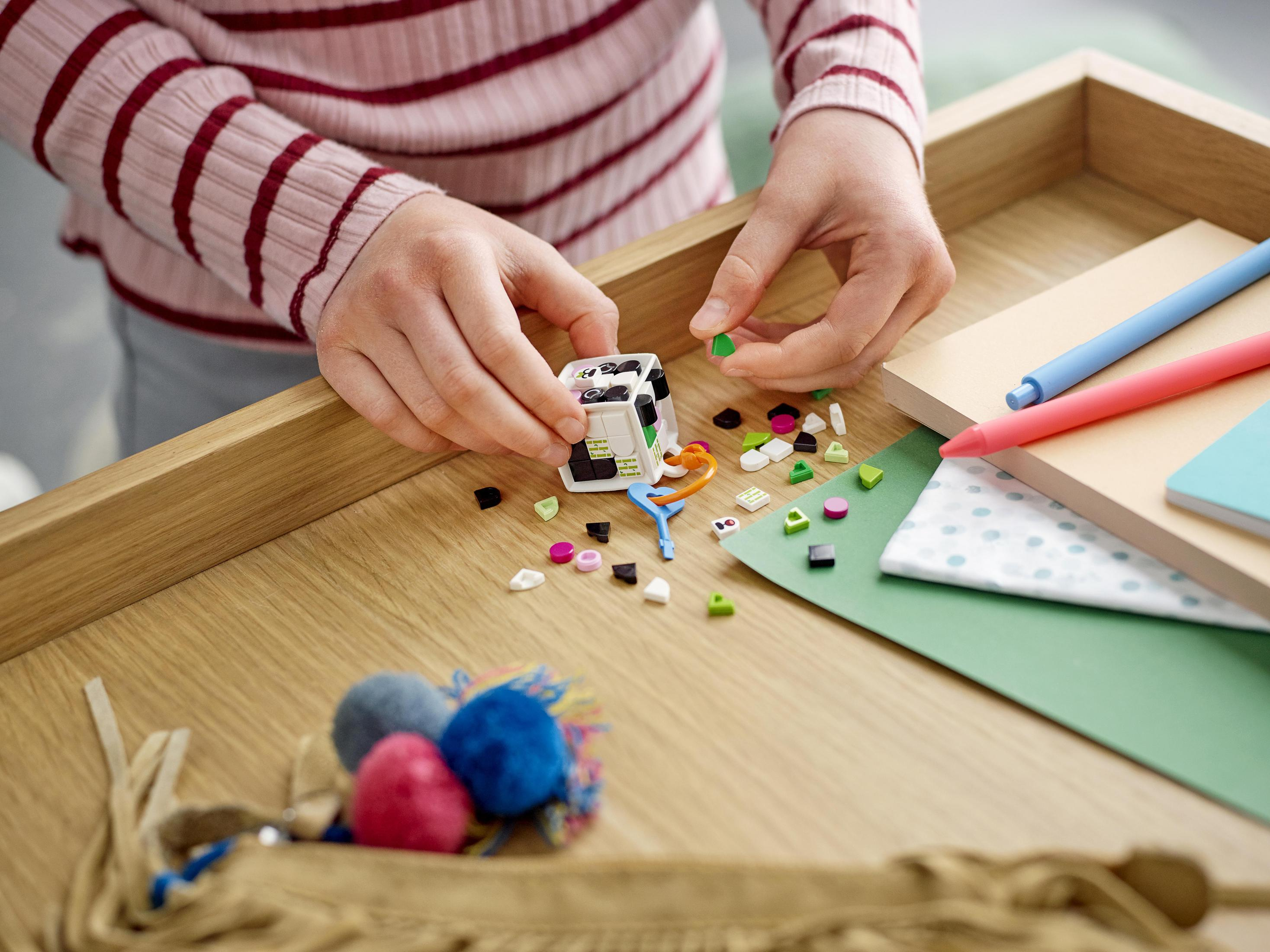 Hände einer Person, die ein Spielzeug mit bunten Blöcken auf einer Holzoberfläche zusammensetzt.