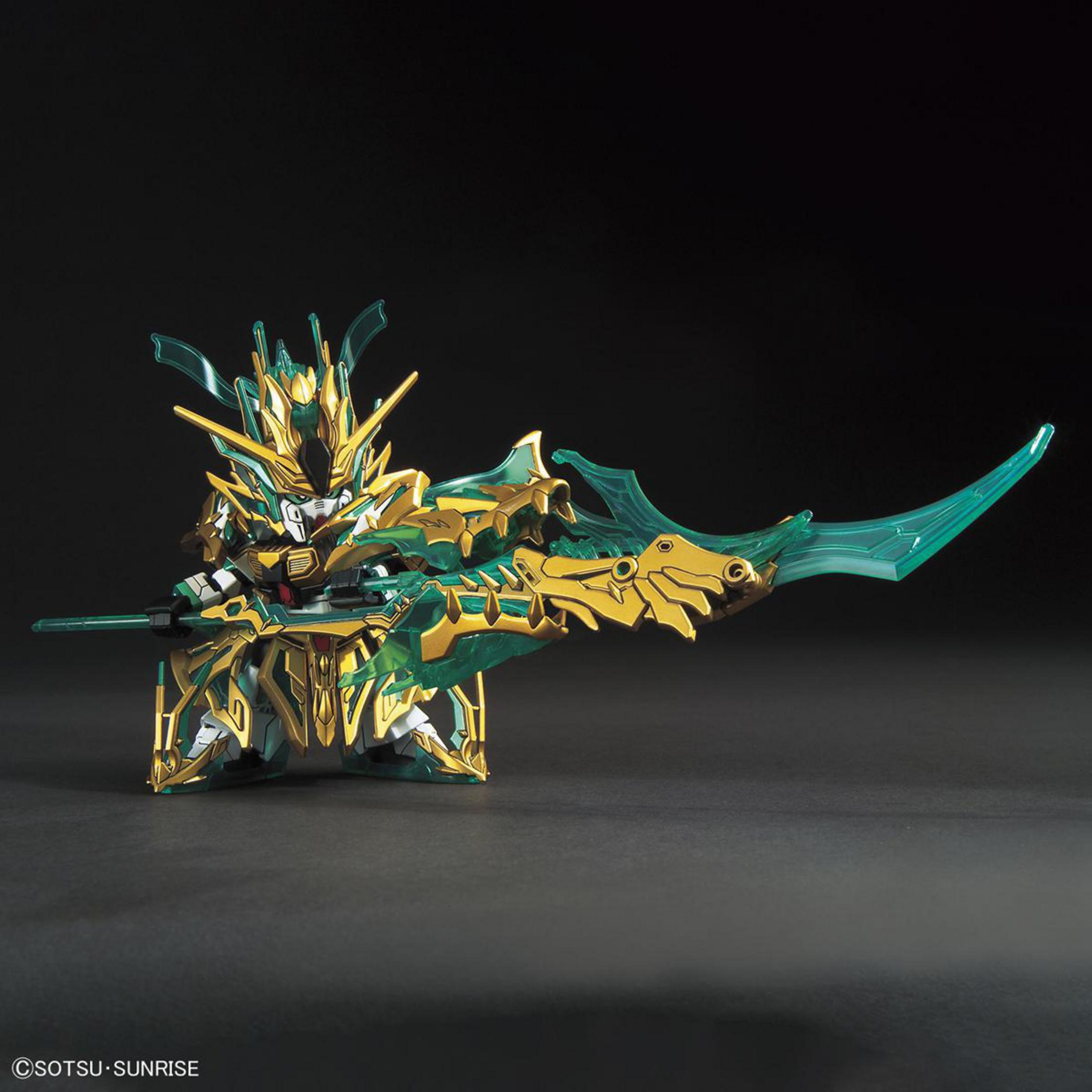 Ein kleines, goldenes und grünes Gundam-Modell mit einem großen Speer und Schild, vor dunklem Hintergrund.