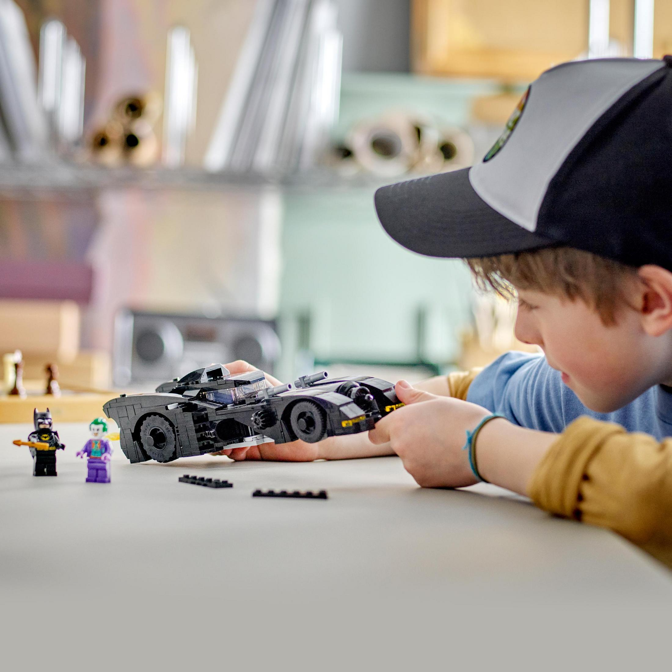 Ein Kind spielt mit einem schwarzen LEGO Batmobil, mit Batman- und Joker-Figuren.
