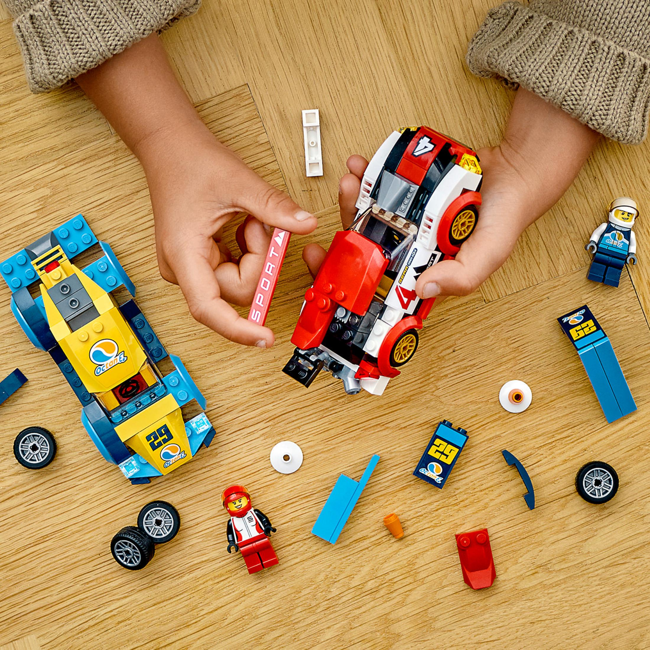 Two toy racing cars being assembled by hands on a wooden surface with loose parts.