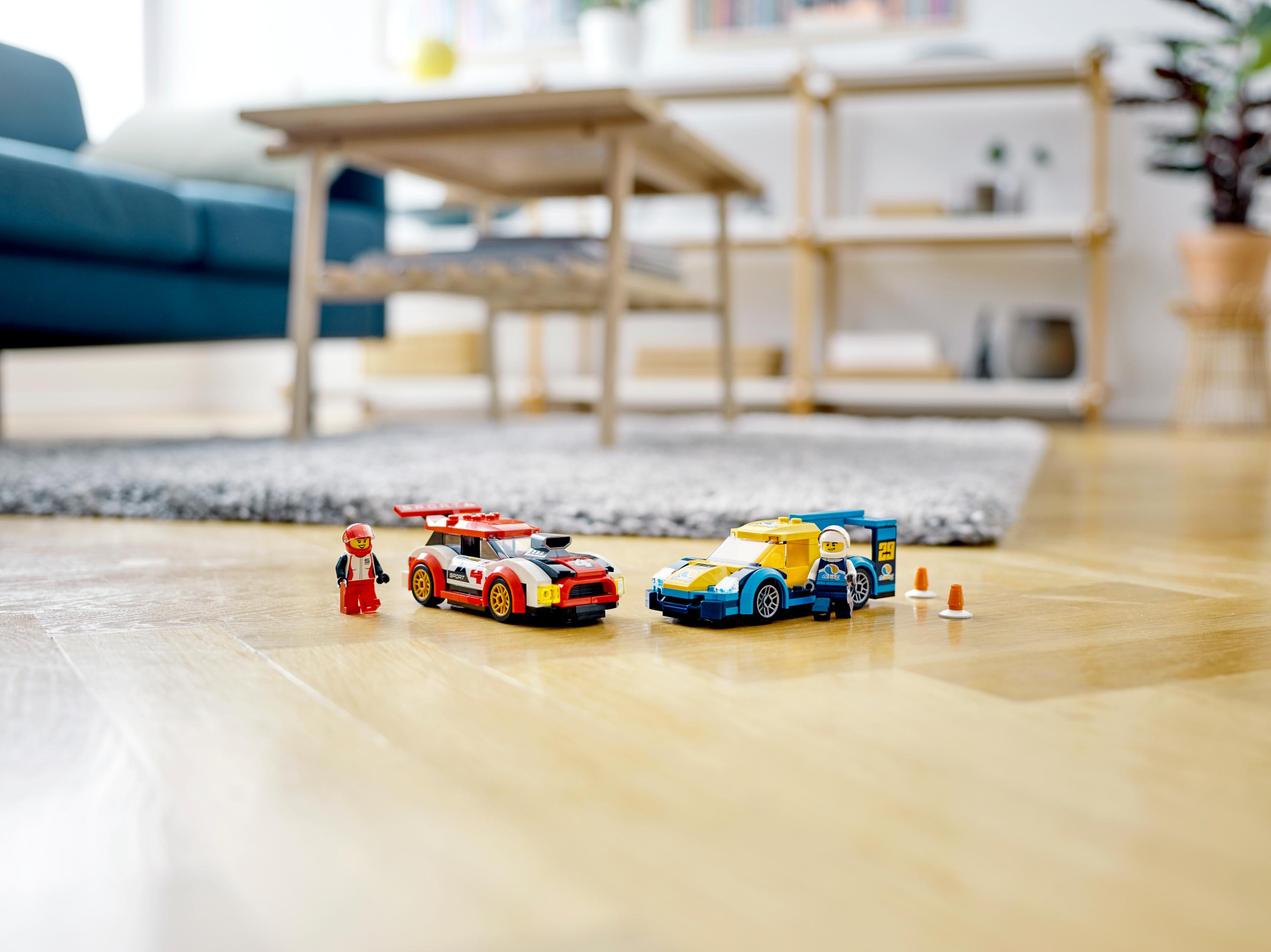 Lego race cars, driver and accessories on a wooden floor. Blurred living room background.