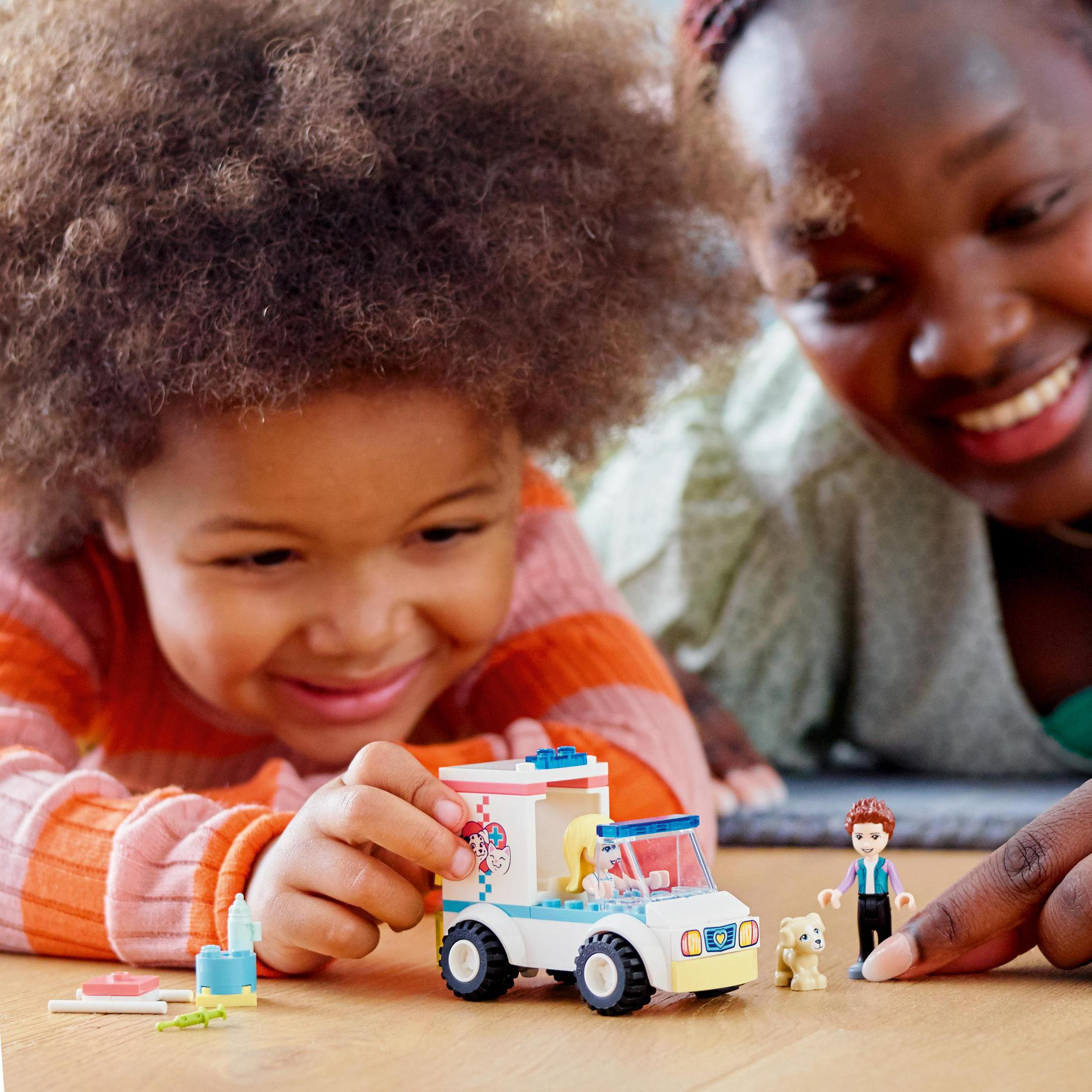 Ein Kind und ein Erwachsener spielen mit einem Lego-Krankenwagen-Set. Es gibt auch ein Hundespielzeug und Figuren.