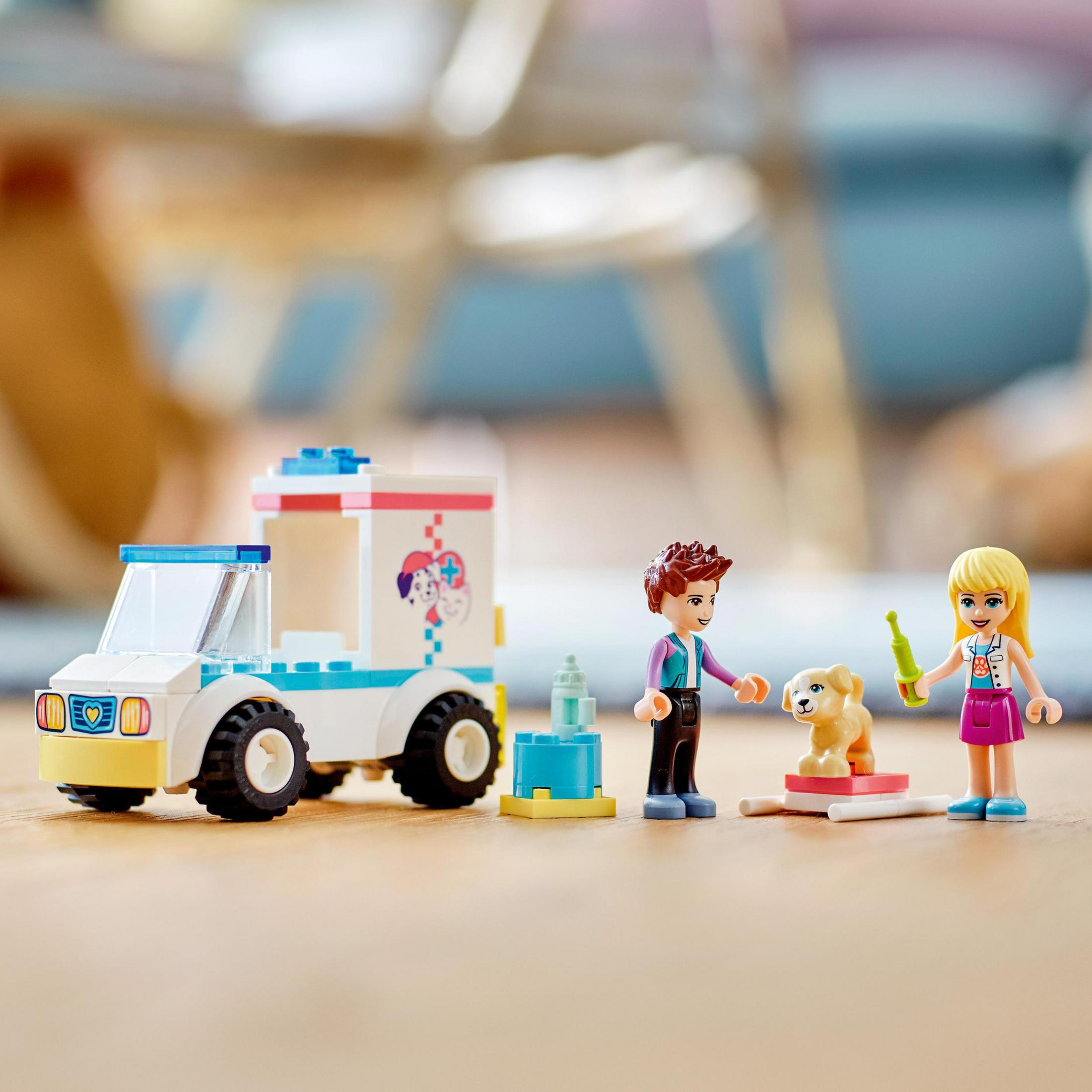 LEGO Friends Set mit Tierklinik, zwei Figuren, einem Hund und Zubehör auf Holzoberfläche.