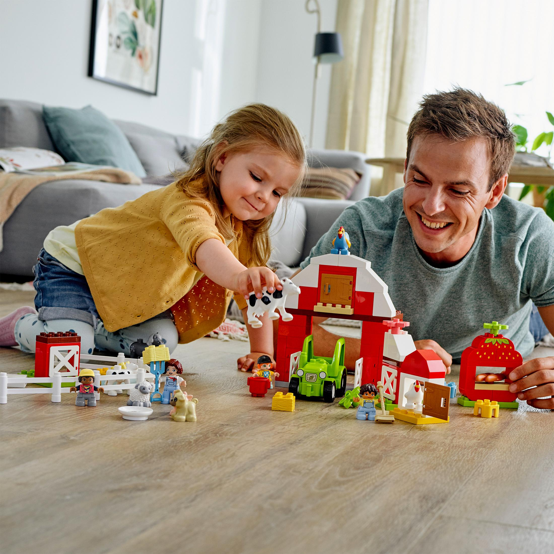 Ein Vater und Kind spielen mit einem Bauernhof-LEGO-Set auf Holzboden.