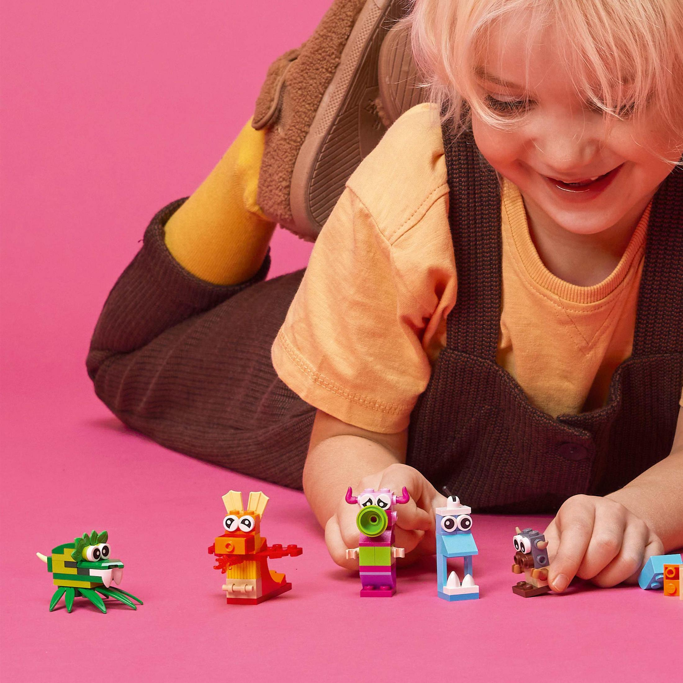 Bir çocuk Lego canavarlarla oynuyor. Pembe bir arka plan üzerinde dört renkli Lego canavar figürü. Çocuk gülümsüyor.
