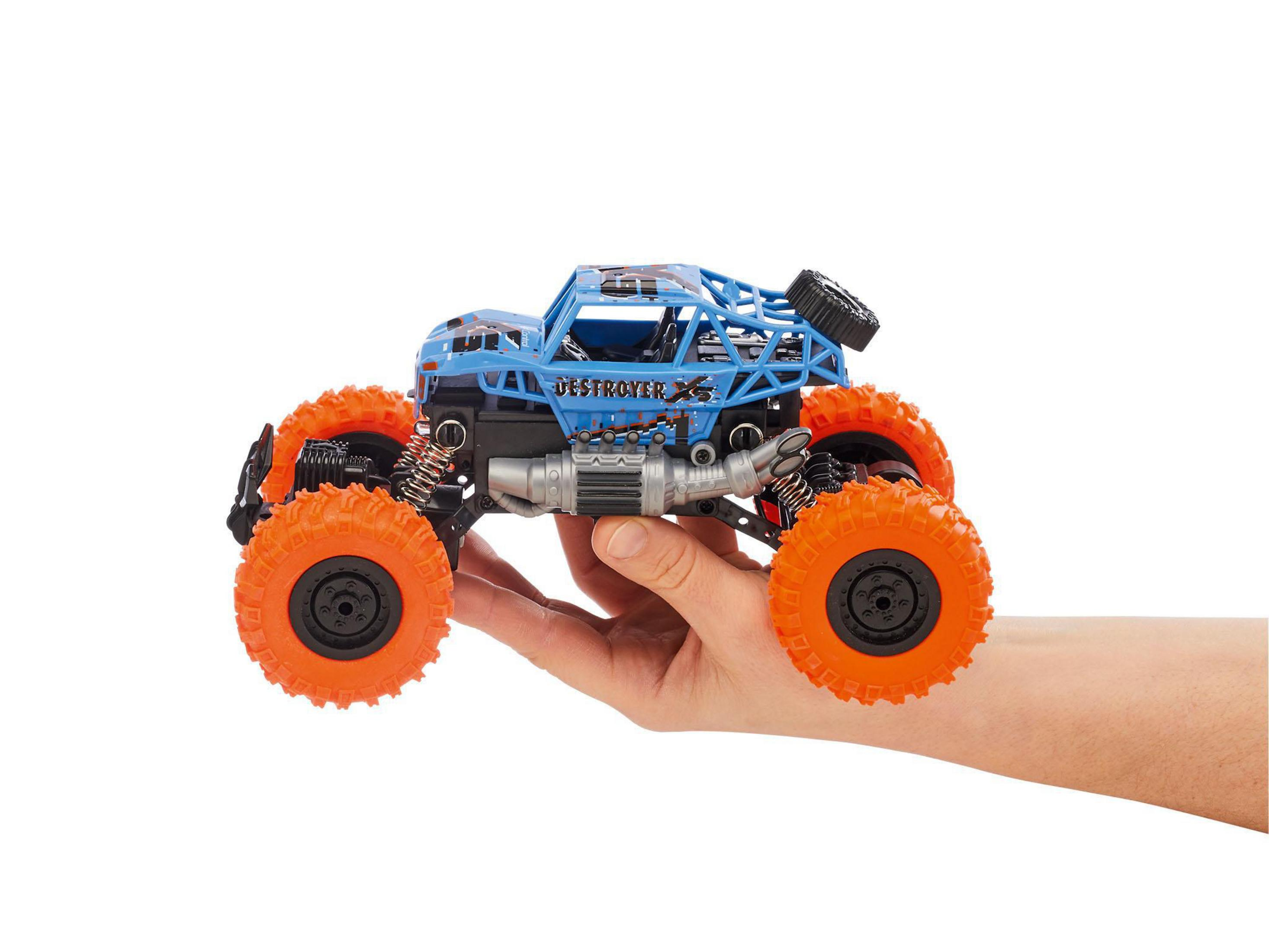 Un monster truck azul y negro sobre fondo blanco, sostenido en la mano de una persona.