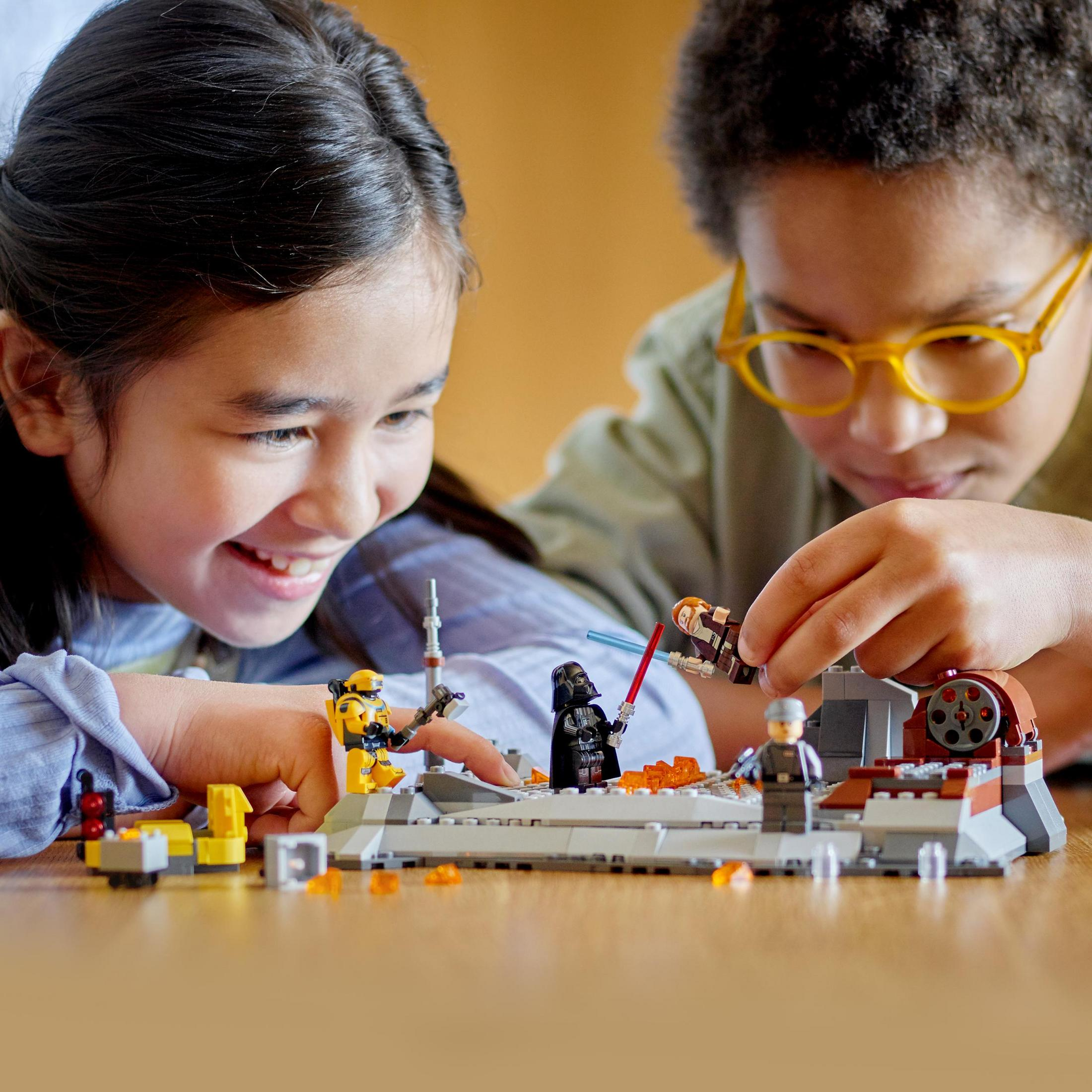 Kinder spielen mit einem Lego Star Wars Set. Ein Kind hält ein Lichtschwert über einer Darth Vader Figur.