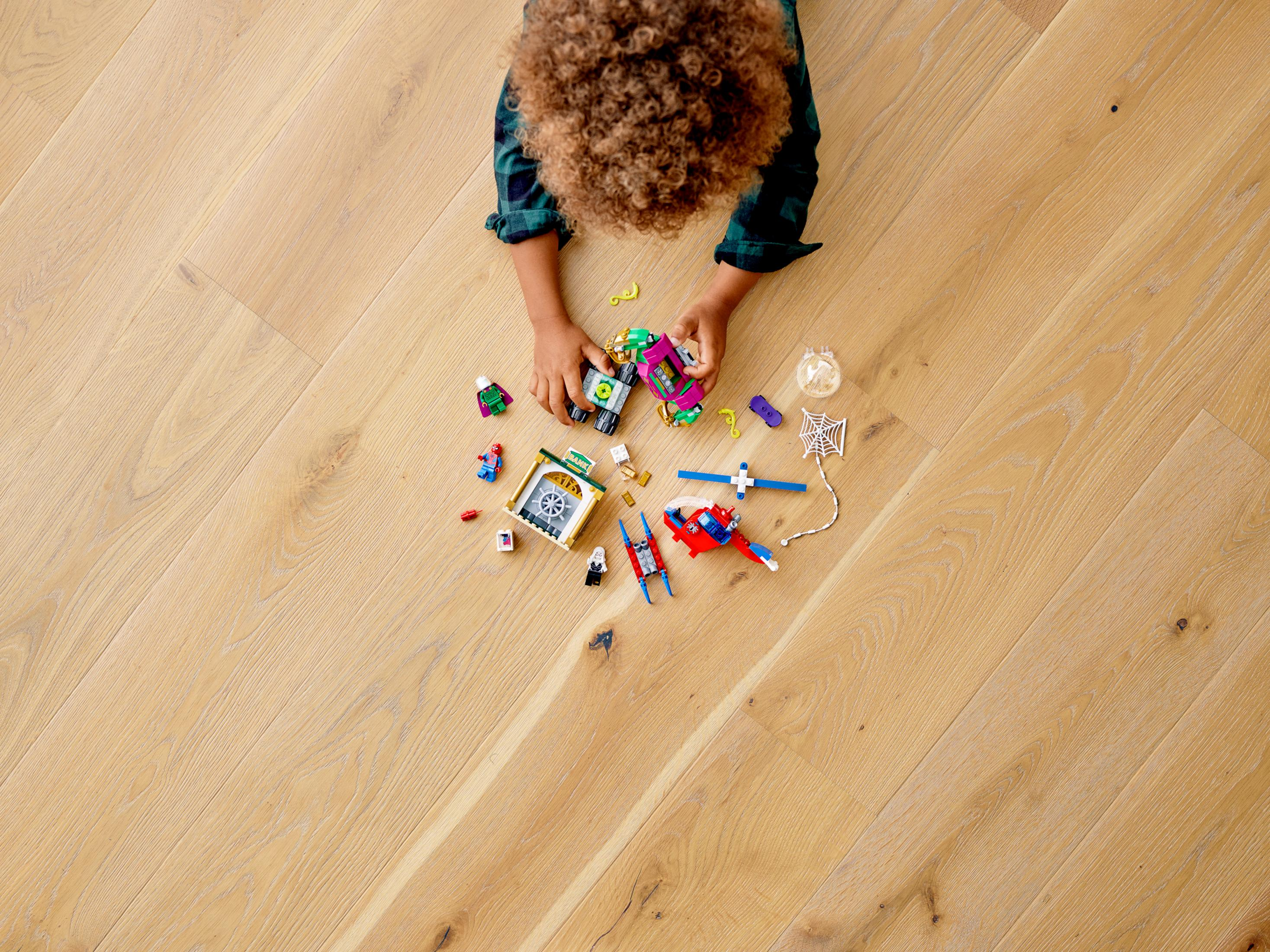 Ein Kind spielt mit Lego auf einem Holzboden. Legoteile und eine Lego Spider-Man Figur sind verstreut.