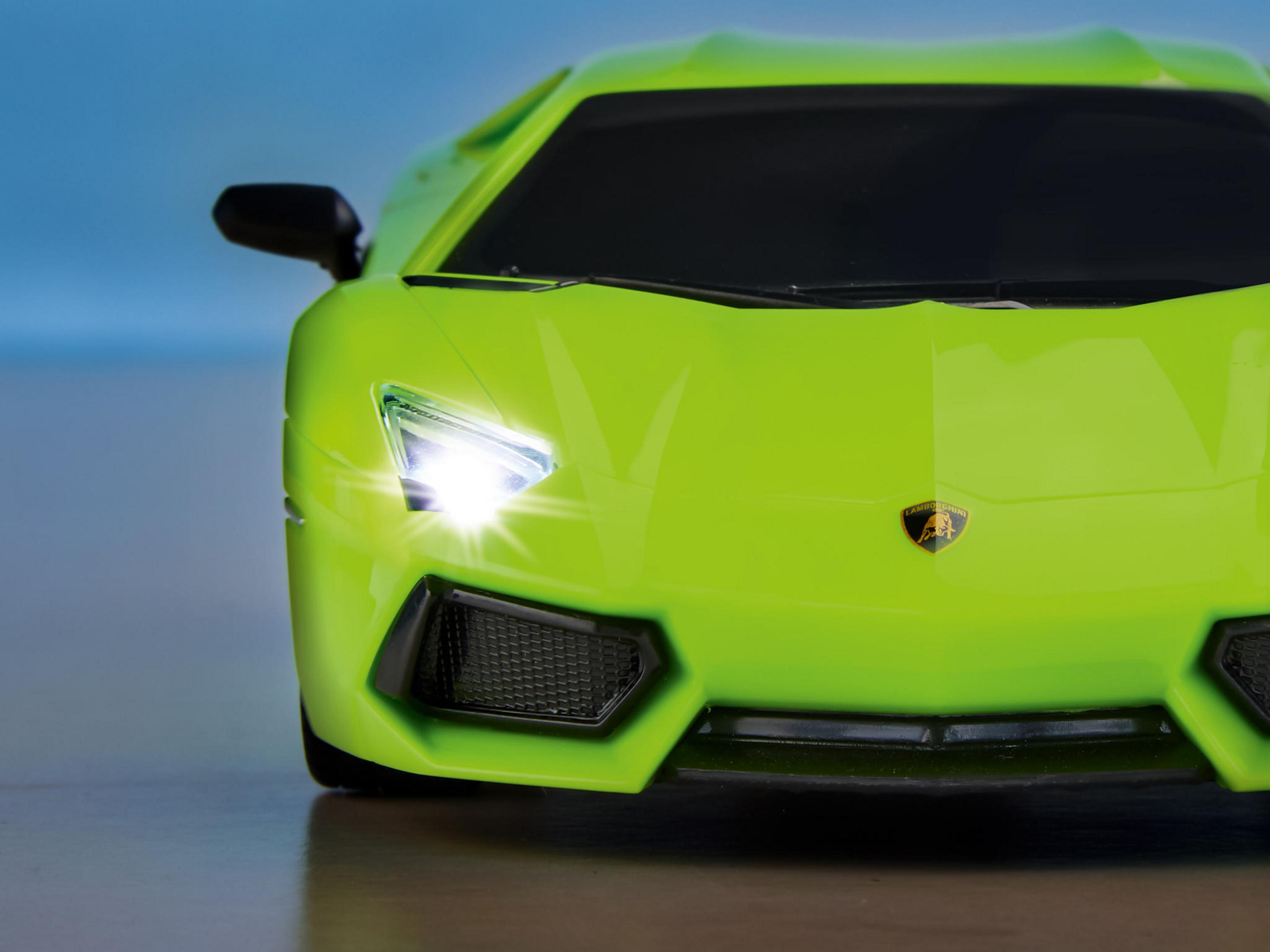 Nahaufnahme der Front eines grünen Lamborghini, Scheinwerfer an, schwarzes Emblem.