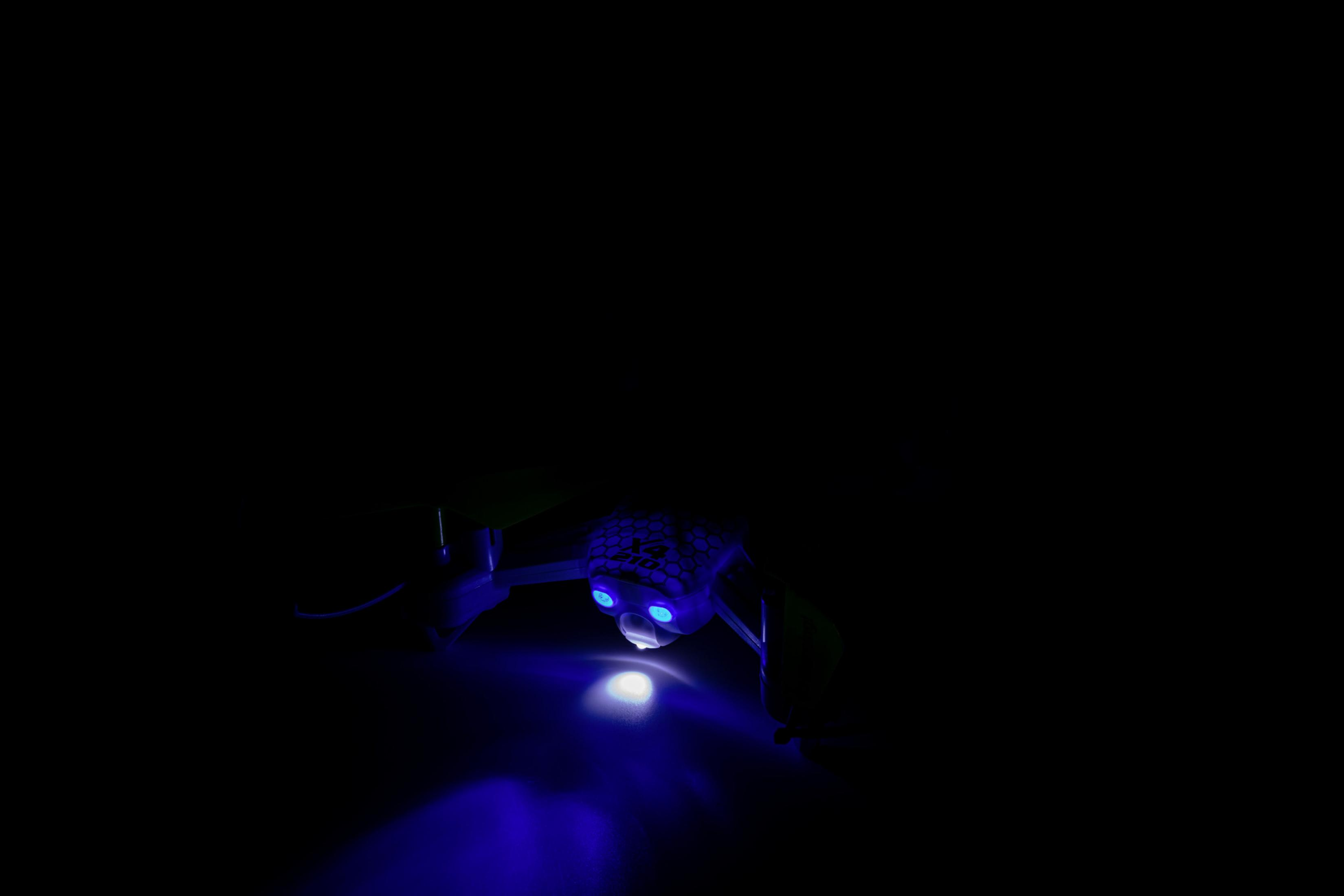 Drohne in dunkler Umgebung mit blauem Licht und leuchtenden Details, vor schwarzem Hintergrund.
