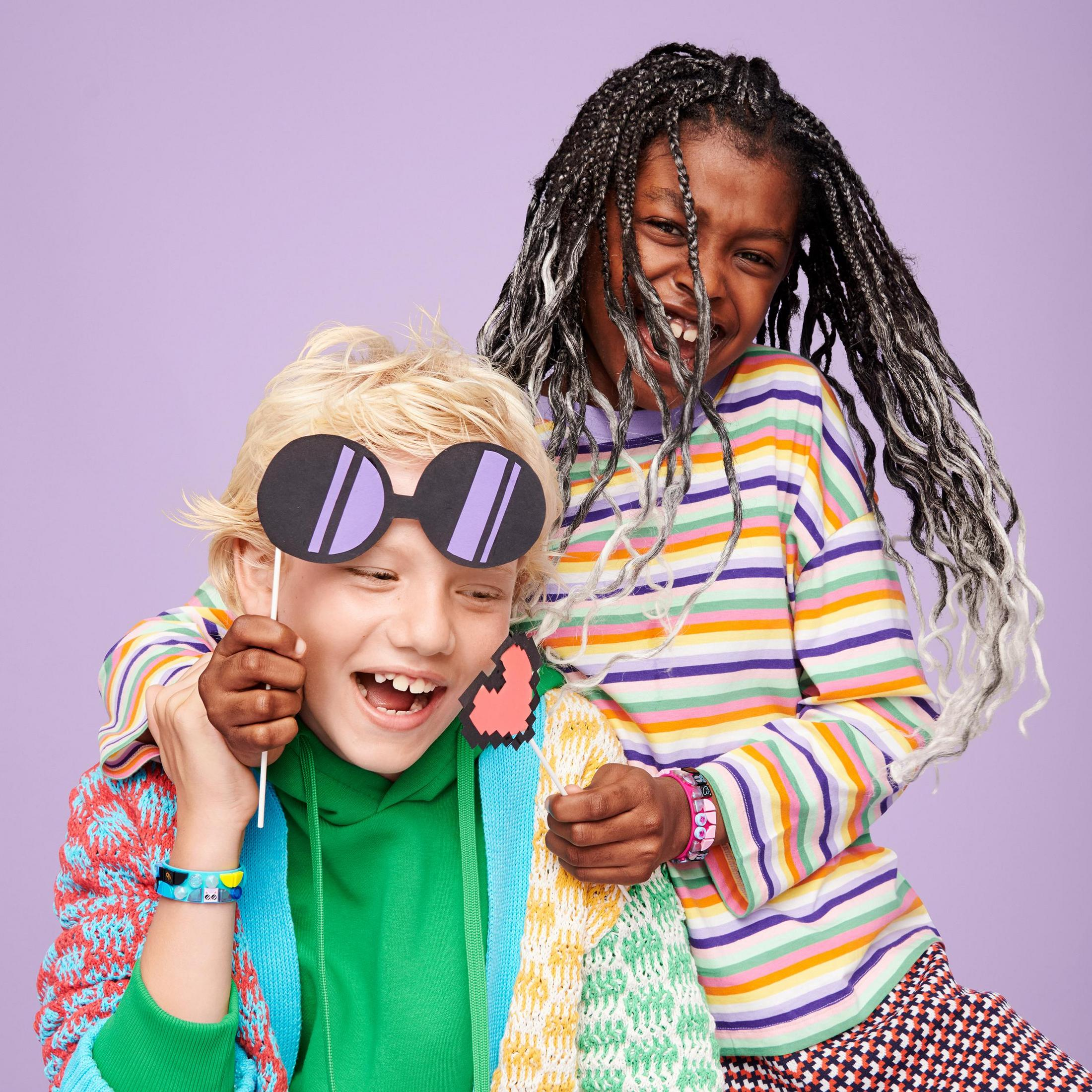 Dwoje dzieci uśmiecha się i śmieje, jedno trzyma duże okulary przeciwsłoneczne, drugie rekwizyt.